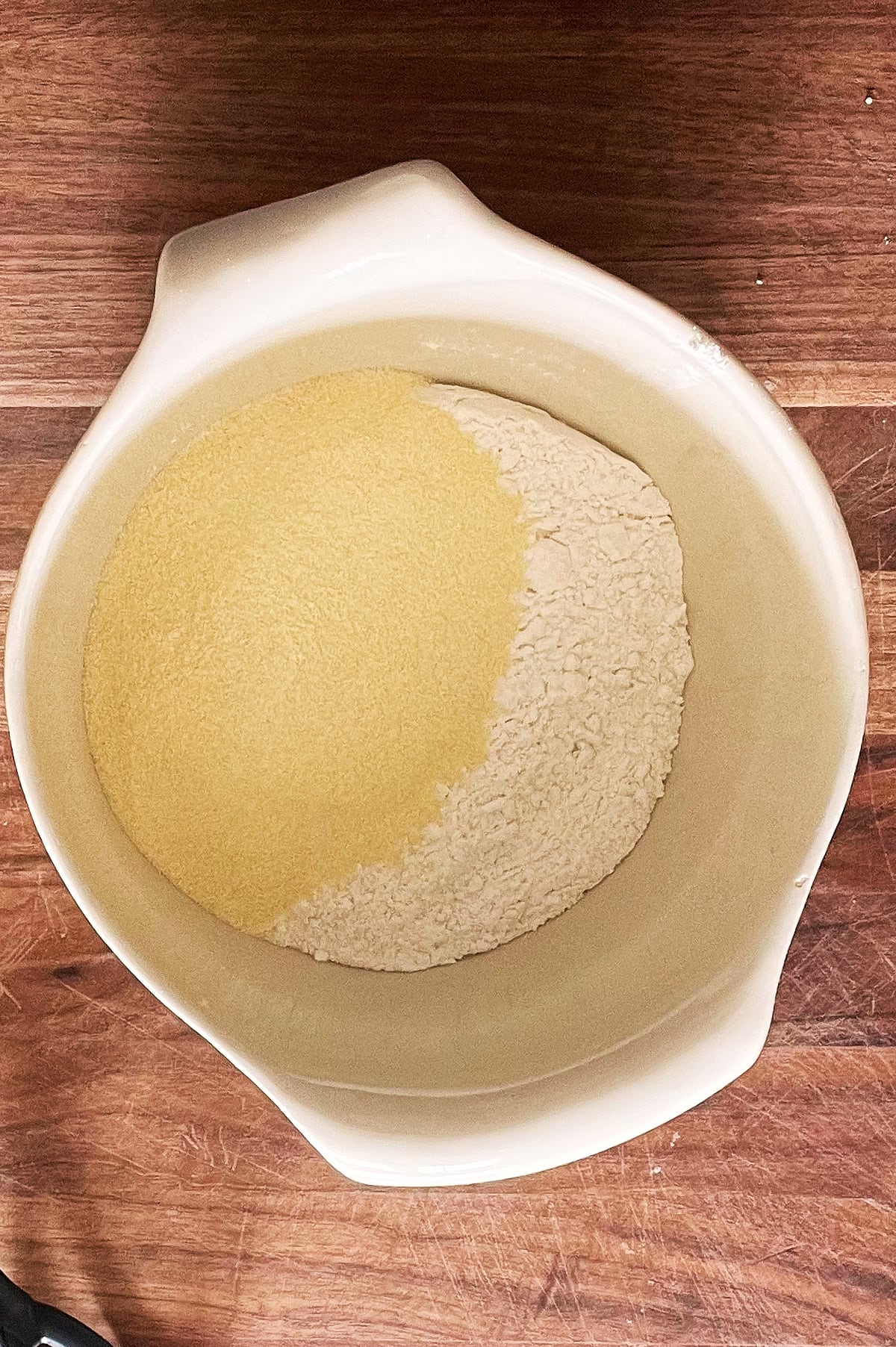 A white bowl with double zero and semolina flour on a wooden board.