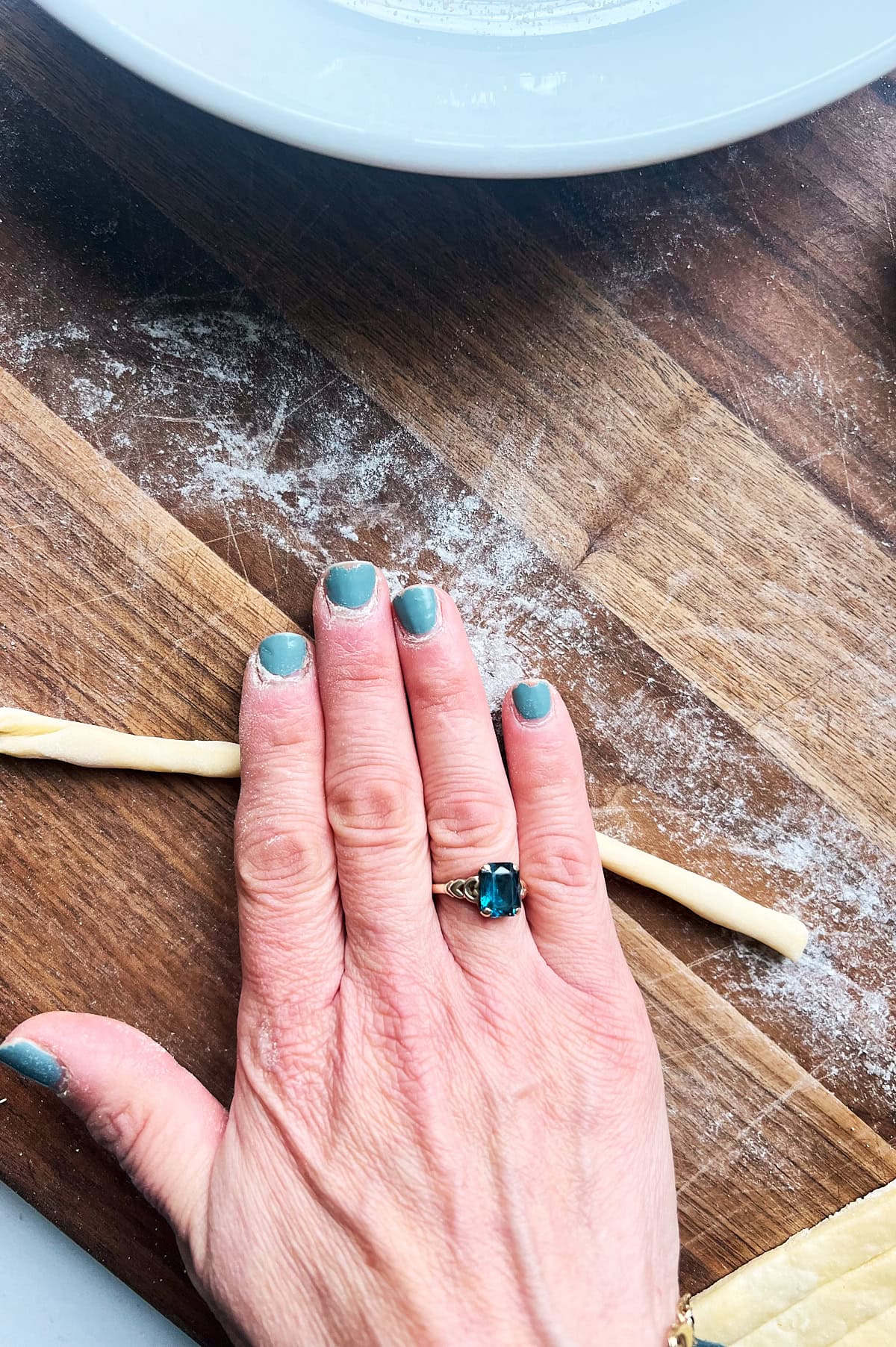 a hand rolling pici noodles from scratch on a wooden board.
