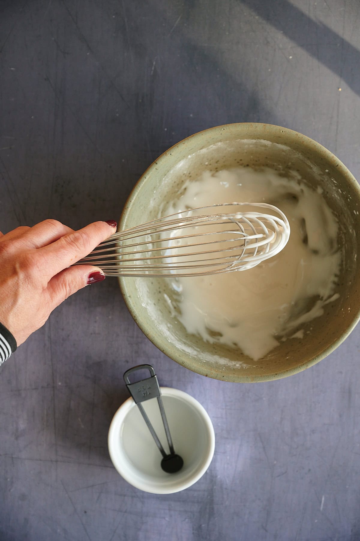 Green bowl of white frosting glaze for raspberry almond cookies