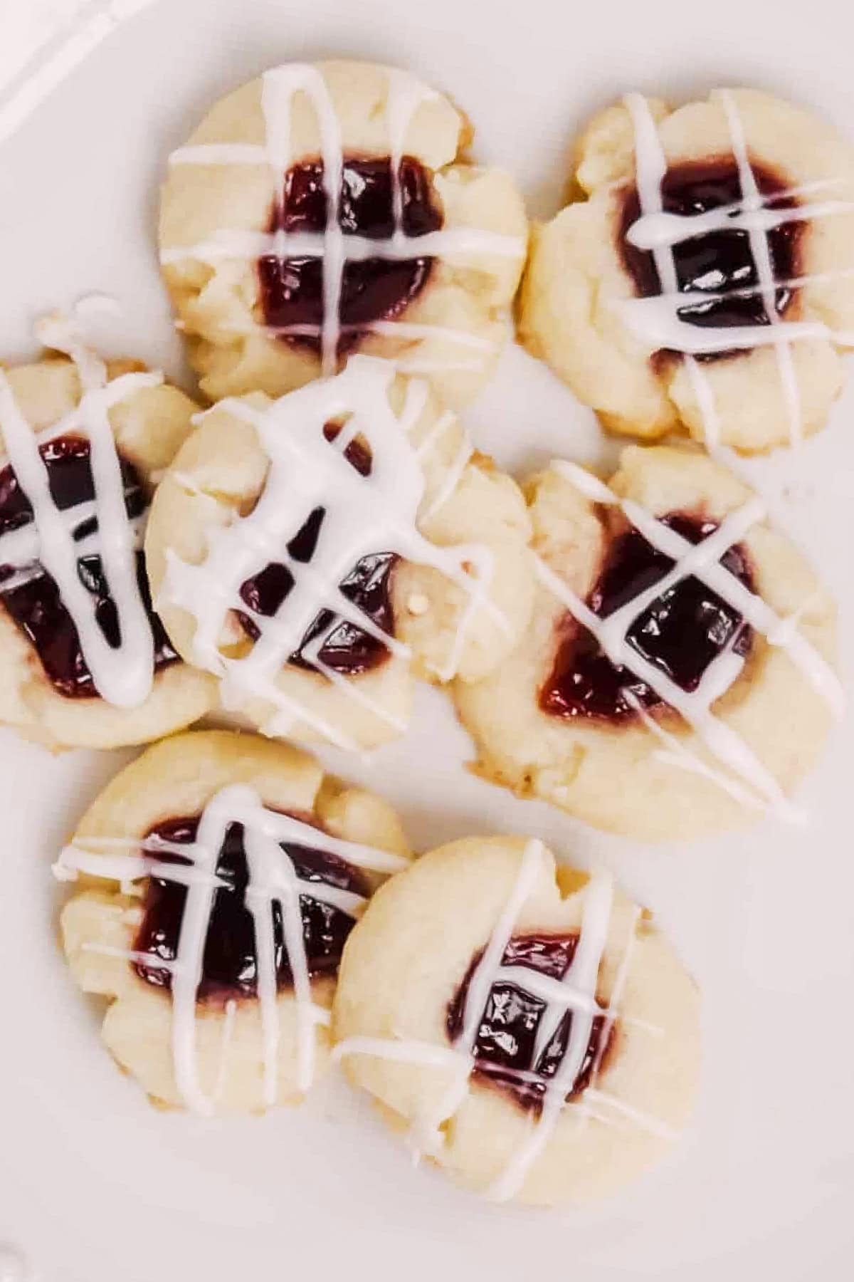 Raspberry almond thumbprints drizzled with white glaze on a white plate.