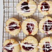 Cooling rack of baked raspberry almond thumbprint cookies glazed with white glaze.