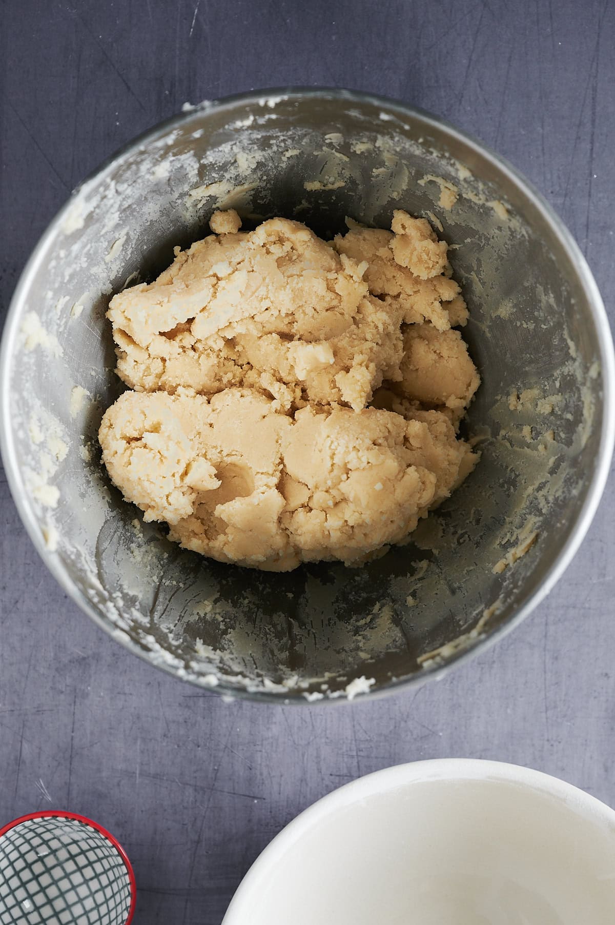 Mixing bowl of cookie dough on a gray background with bowls nearby.