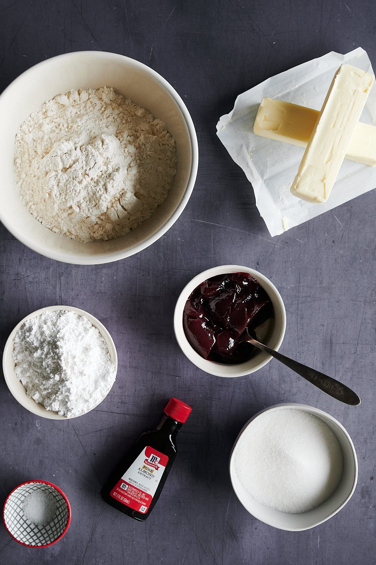 Ingredients for raspberry almond thumbprint cookies on a gray background.