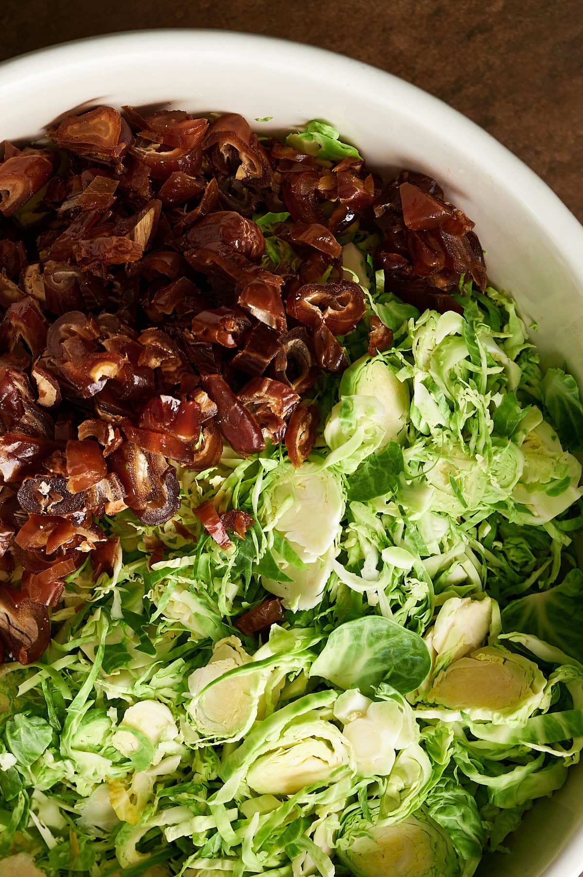 Close up of white bowl with chopped dates and shredded Brussels sprouts.