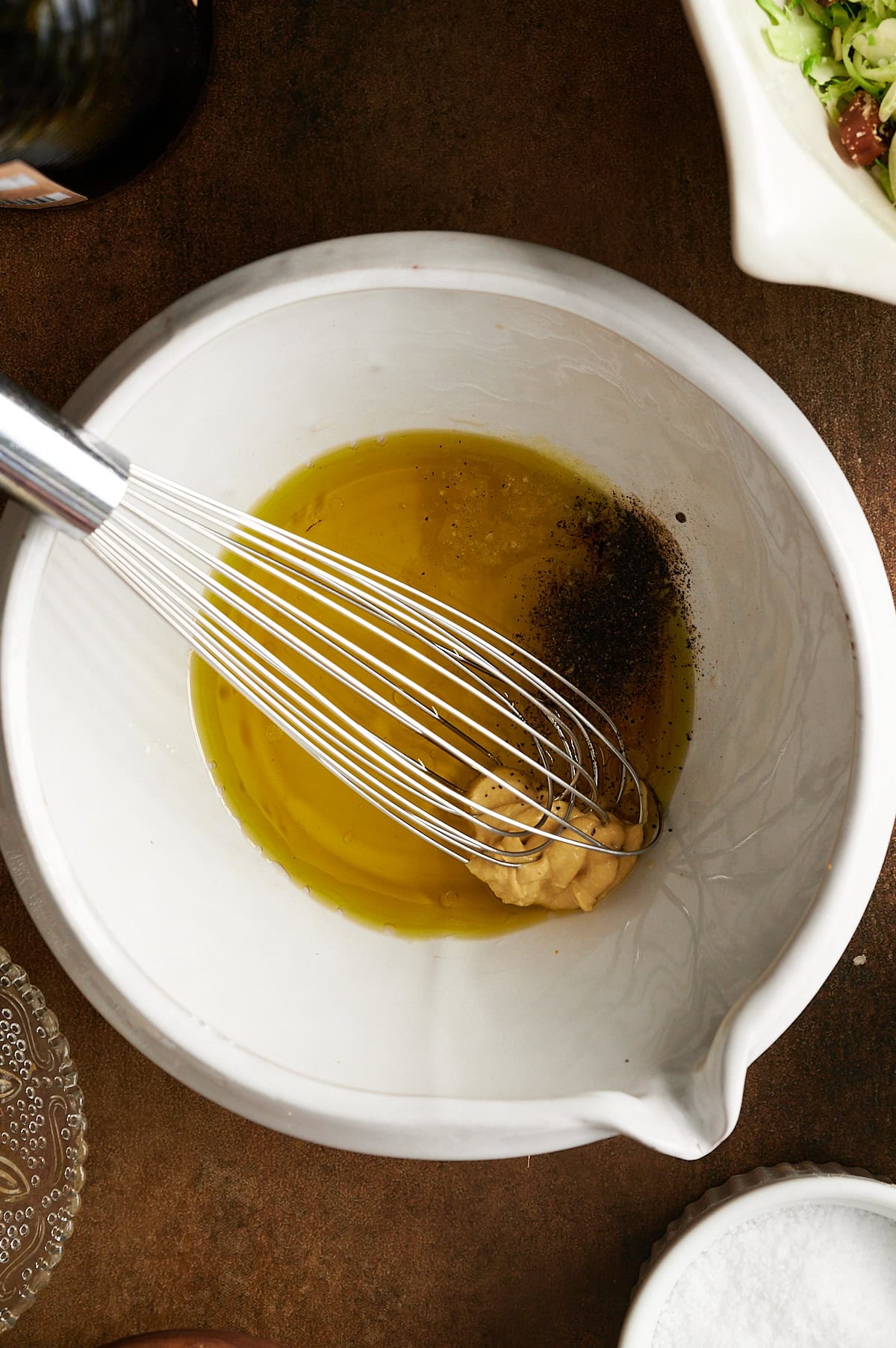 White bowl with salad dressing being whisked on a brown background.