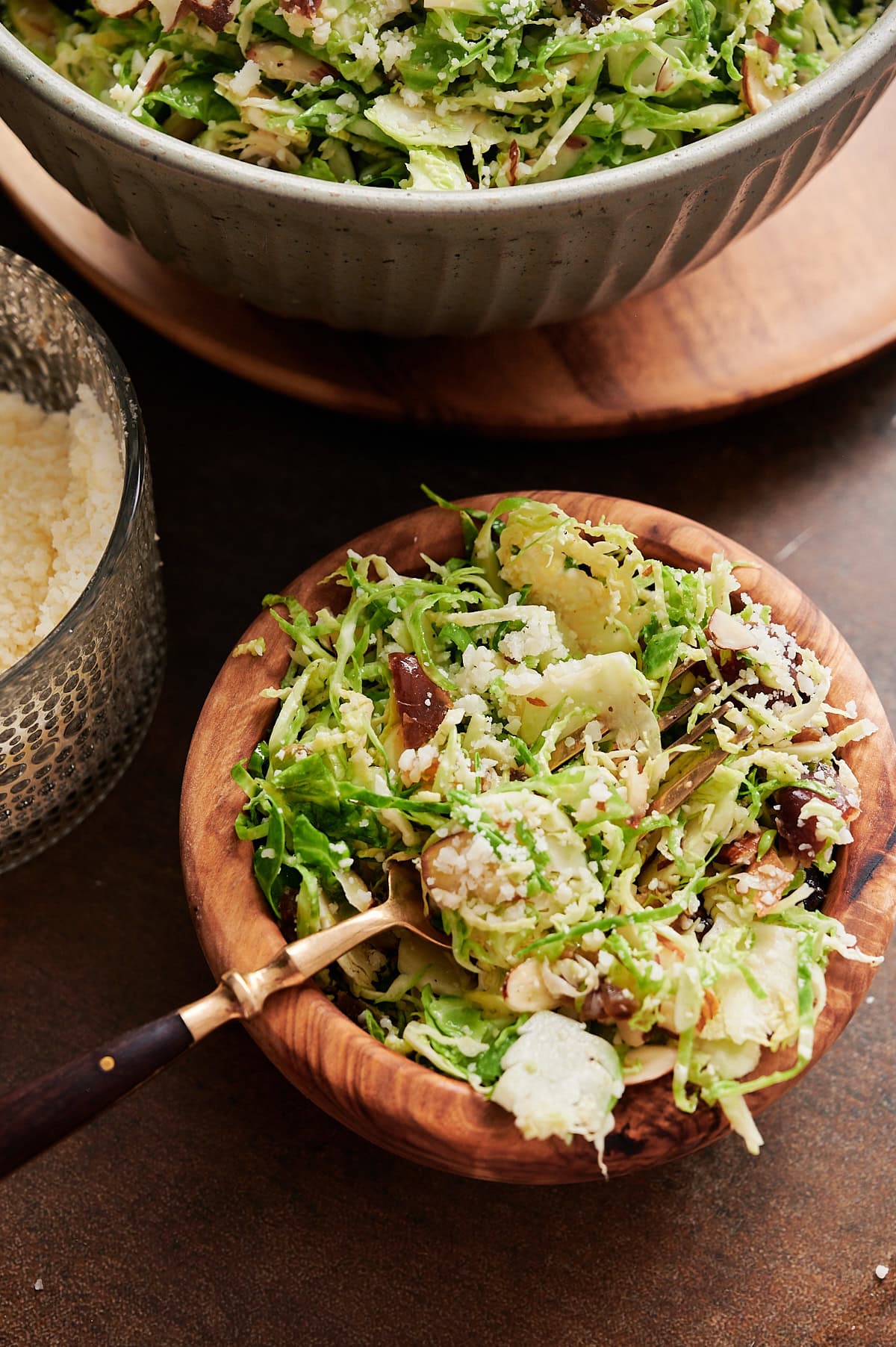 small wooden bowl with shredded Brussels sprouts, dates and parmesan cheese with a spoon tucked in.