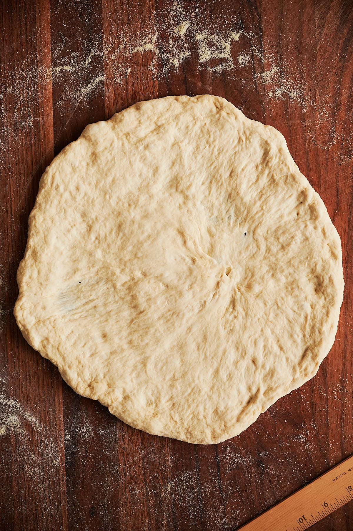 Stretched round of pizza dough on a wooden cutting board with flour.