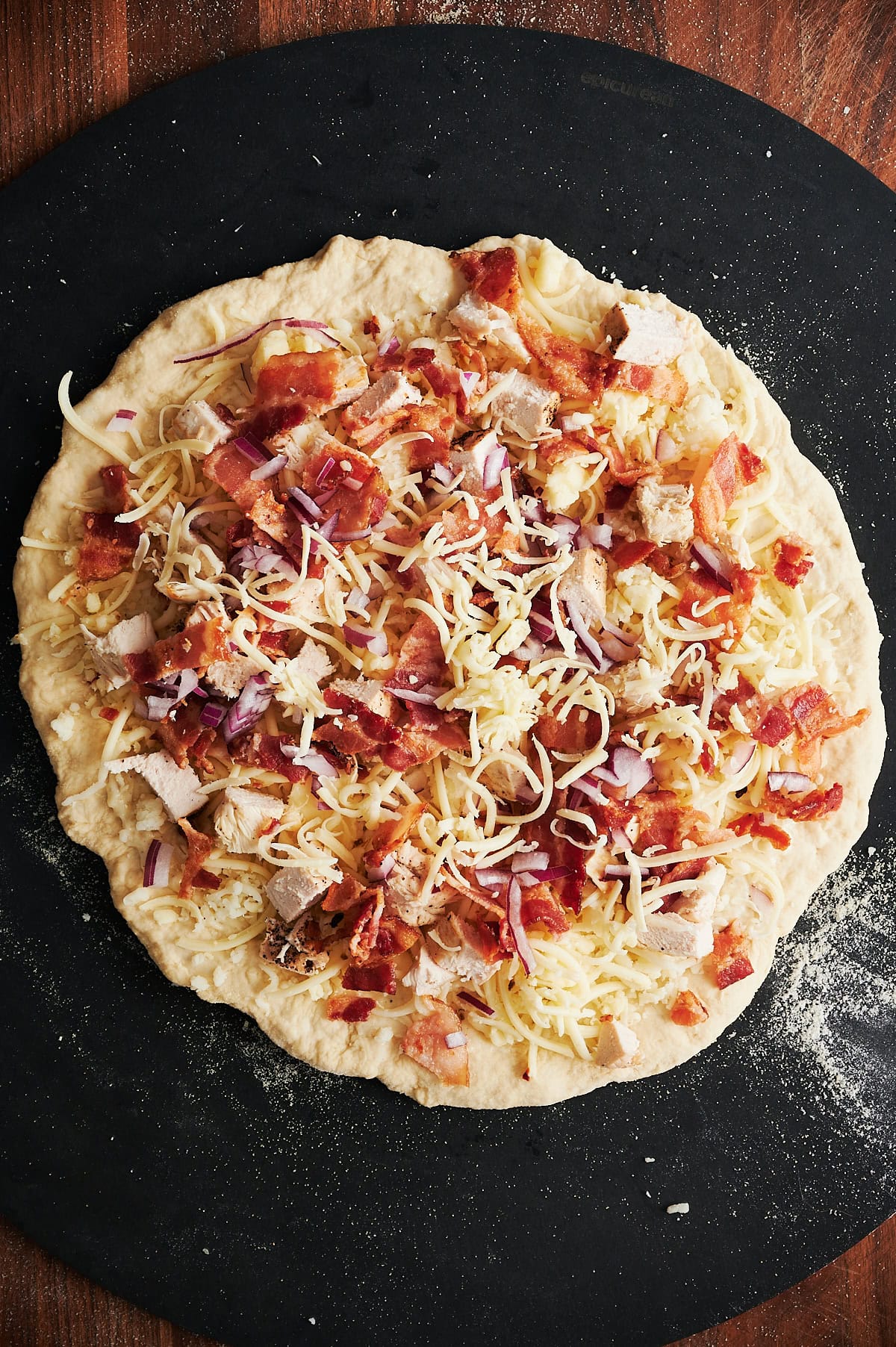 Unbaked chicken bacon pizza on black pizza peel.