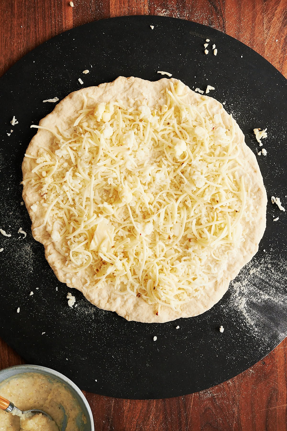 Black pizza peel with pizza dough topped with cheeses.