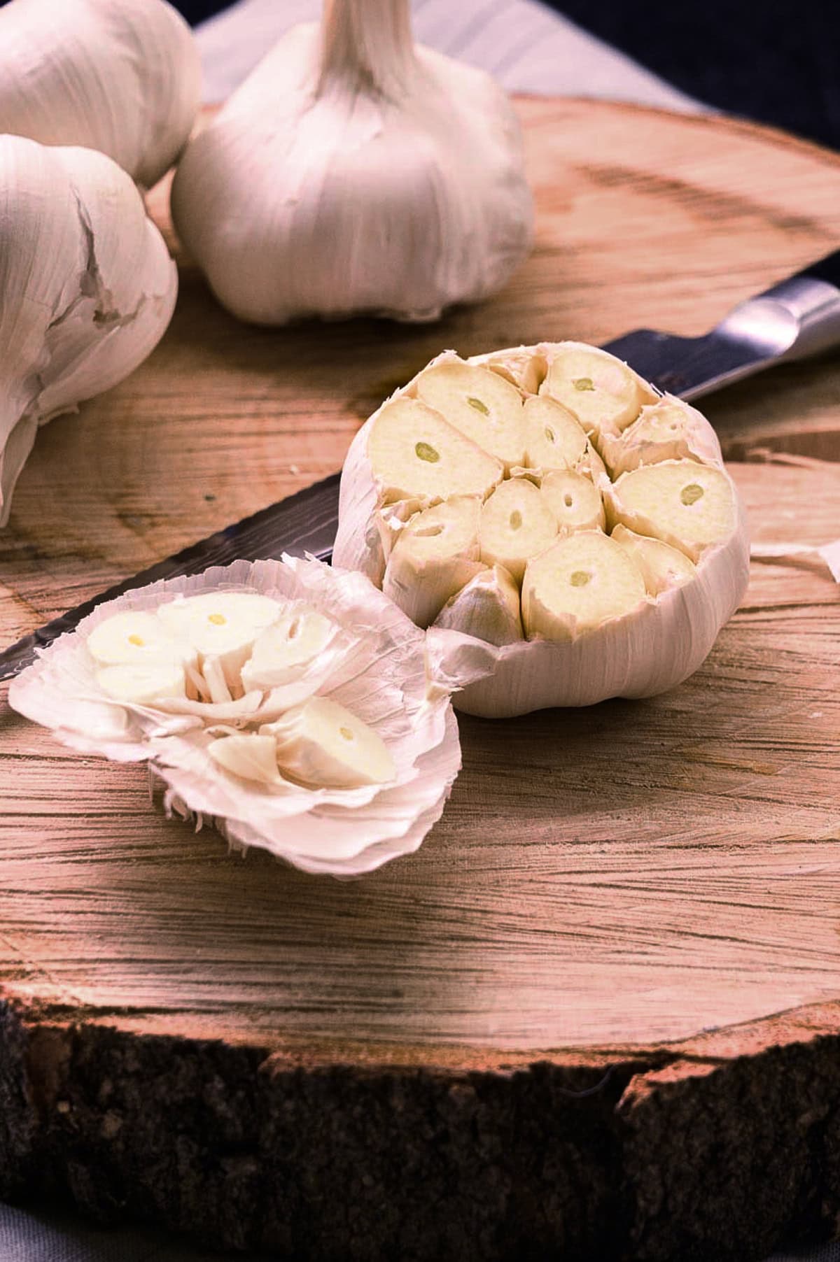 A wooden trivet holding a head of garlic that has been trimmed with a sharp knife to expose the tops of the cloves.