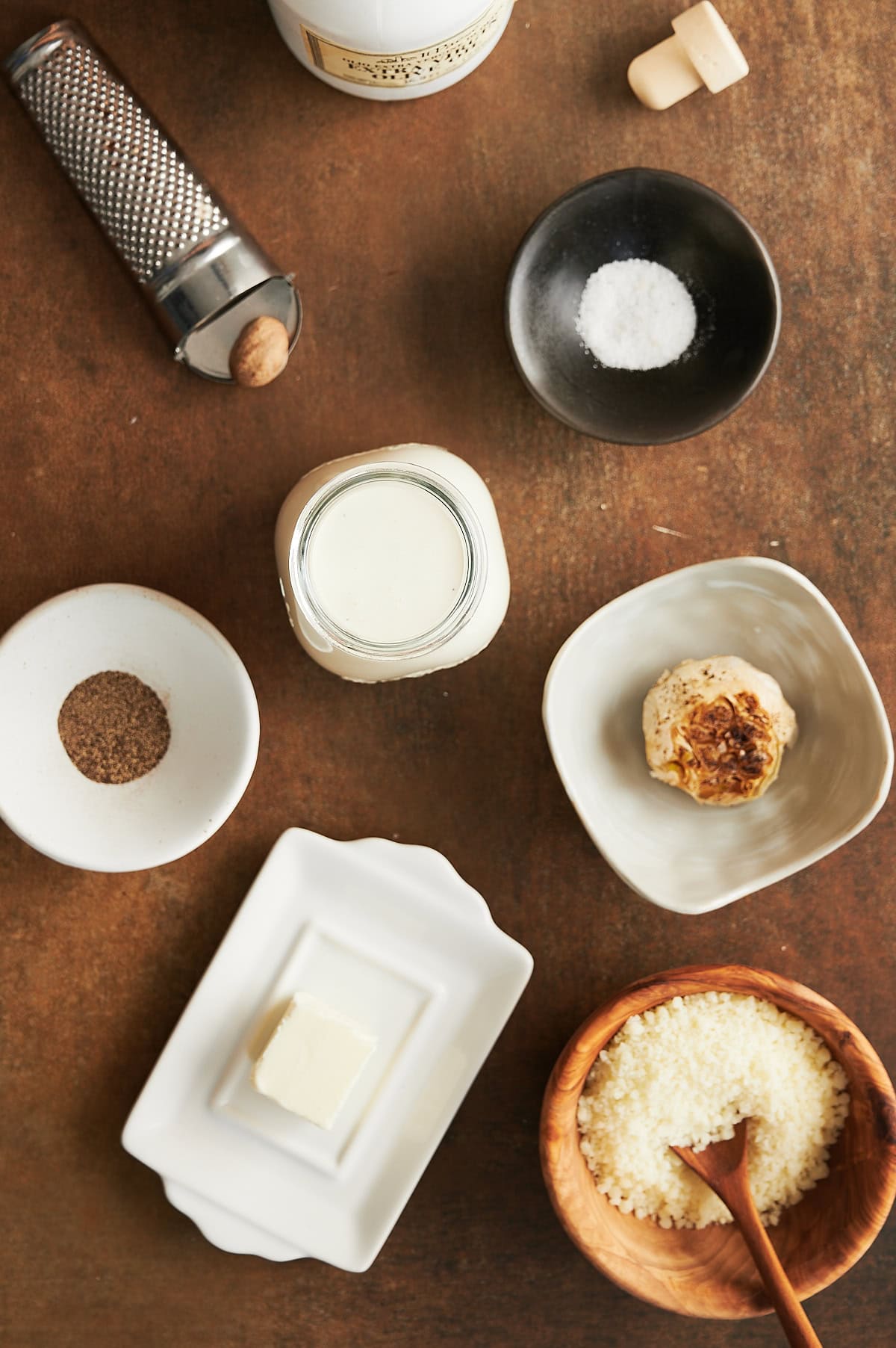Ingredients for creamy roasted garlic pizza sauce in bowls on a brown background.