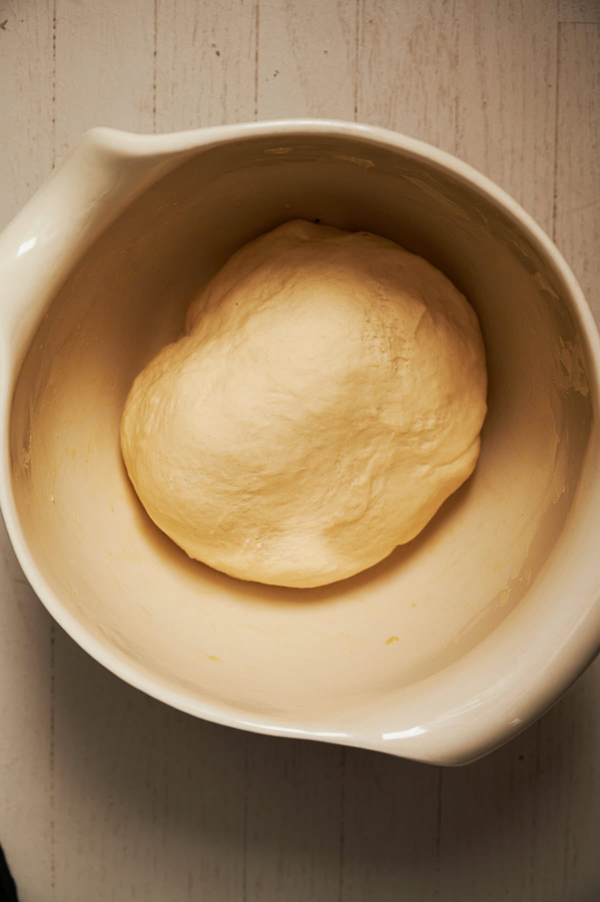 White bowl with risen and rested thin crust pizza dough.