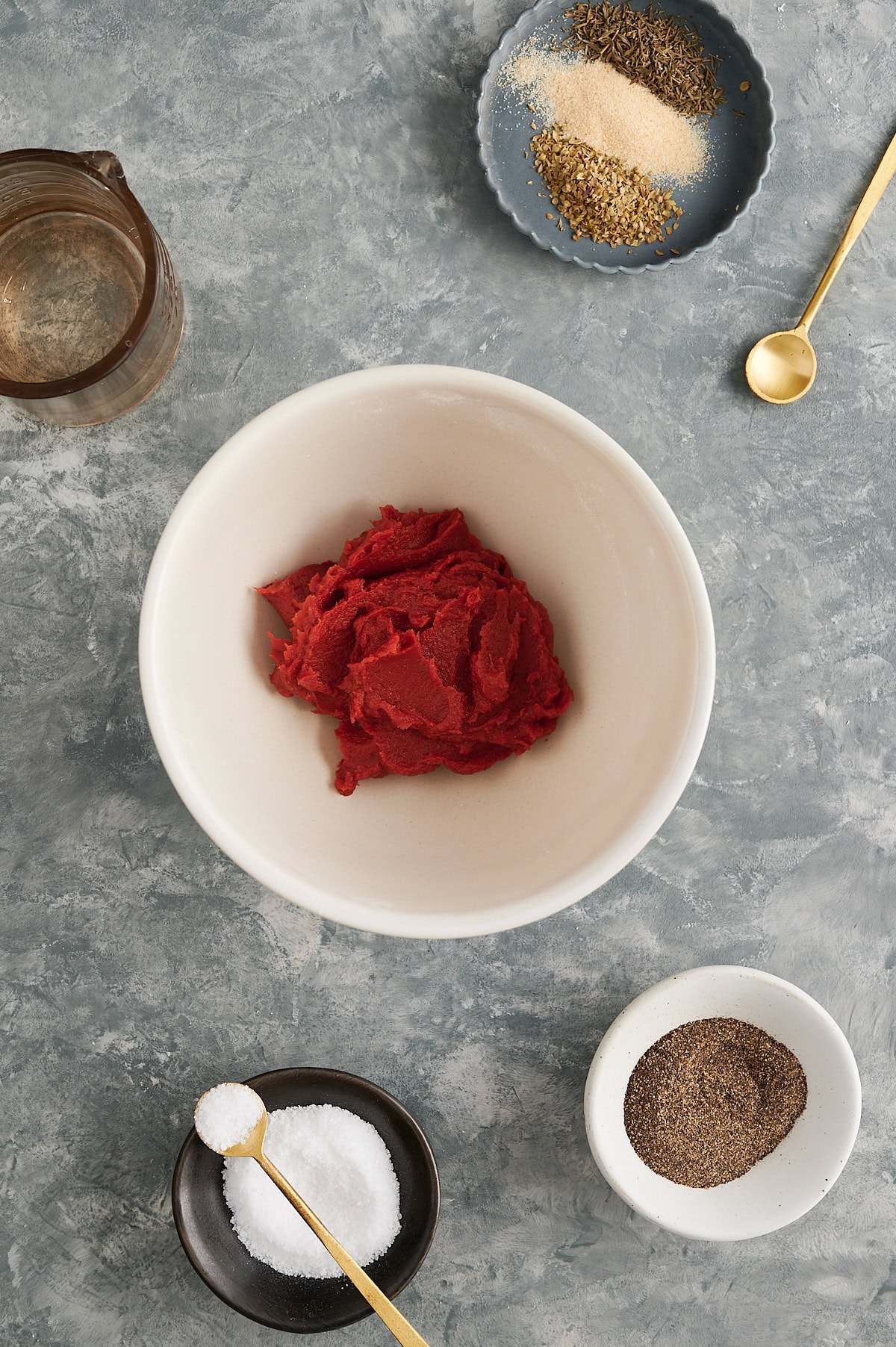 Ingredients like seasoning for tomato paste pizza sauce in white bowls on a gray background.