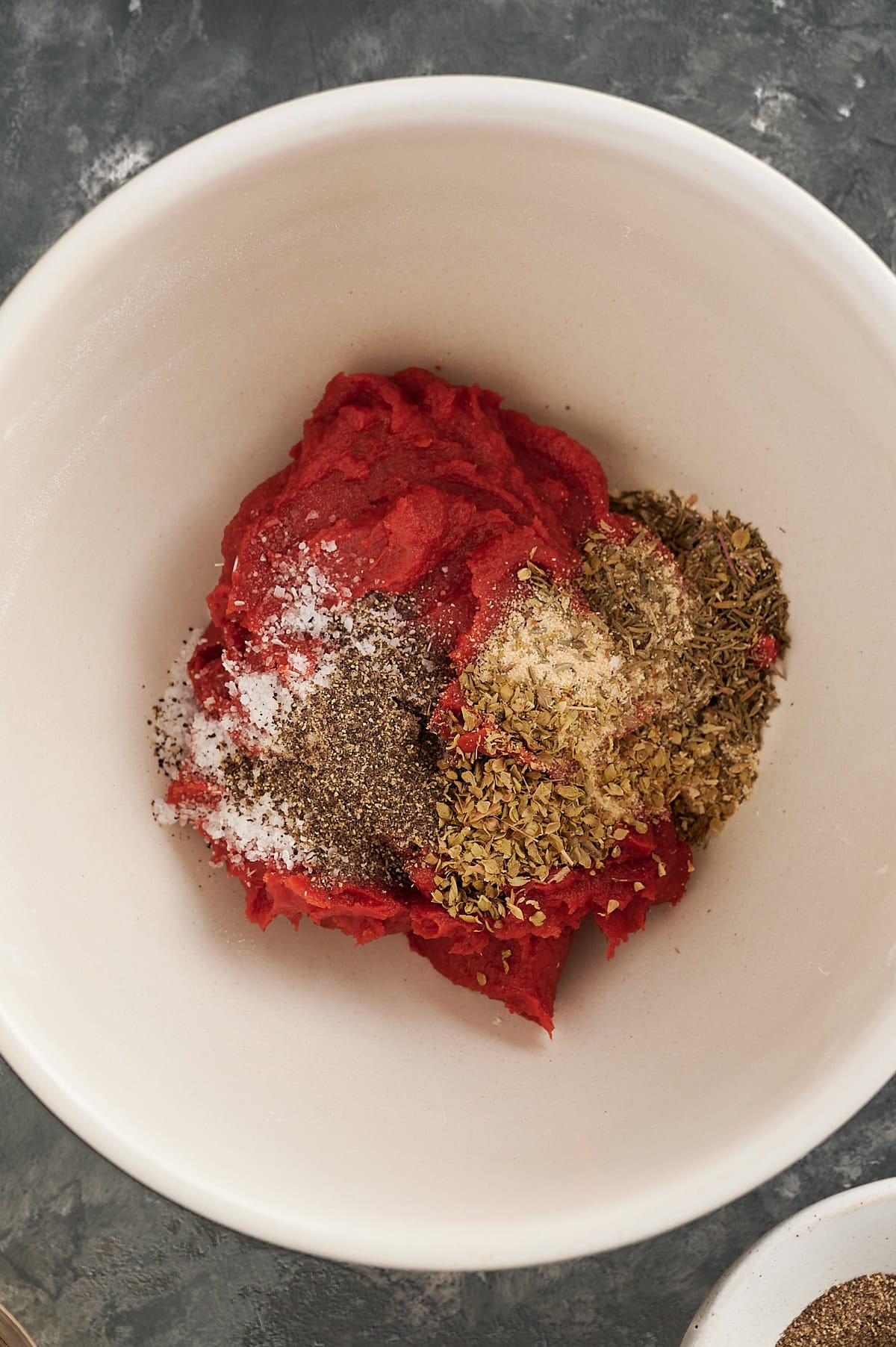 White bowl with tomato paste, herbs, and seasoning for pizza sauce.