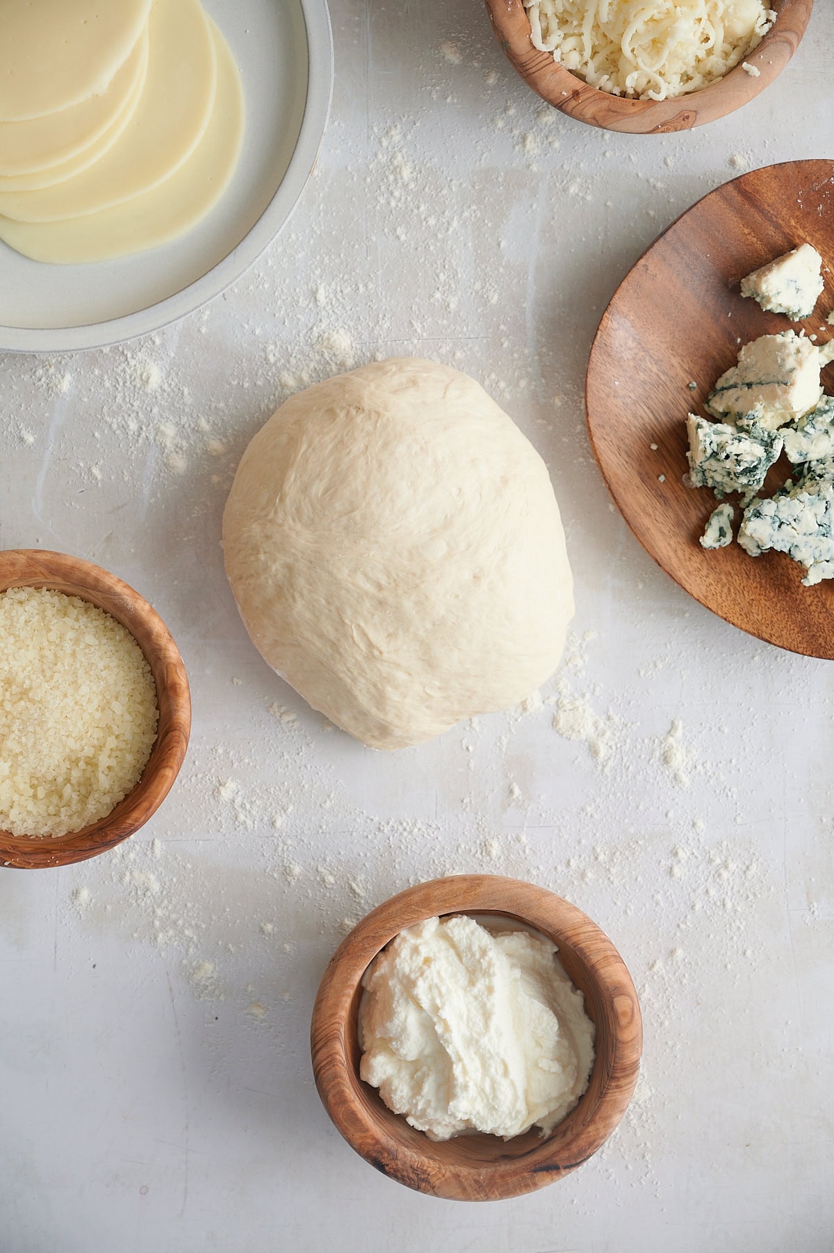 Pizza dough surrounded by gruyere, fontina, gorgonzola, parmesan, ricotta, mozzarella and provolone on a white background.