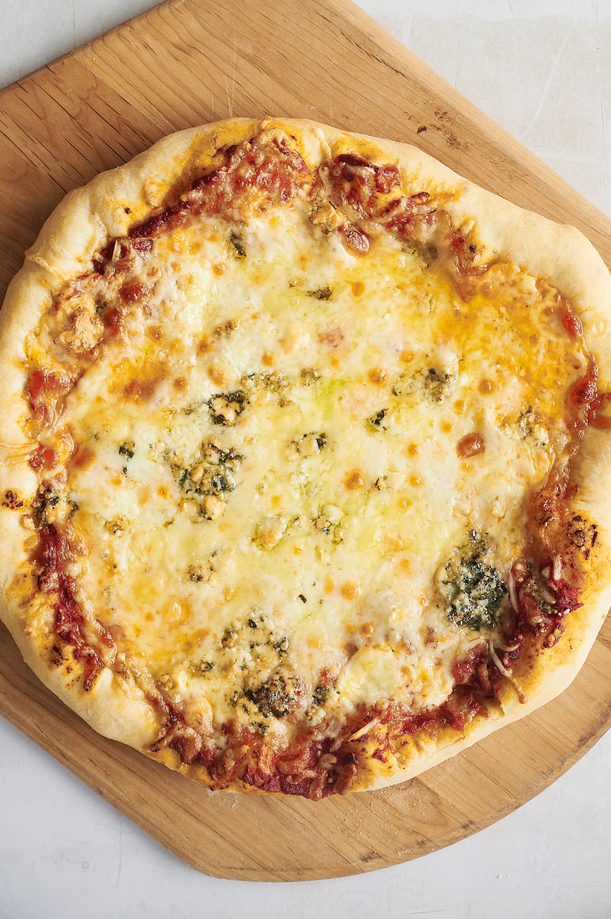 Baked 7 cheese pizza with gorgonzola on a wooden pizza peel and white background.