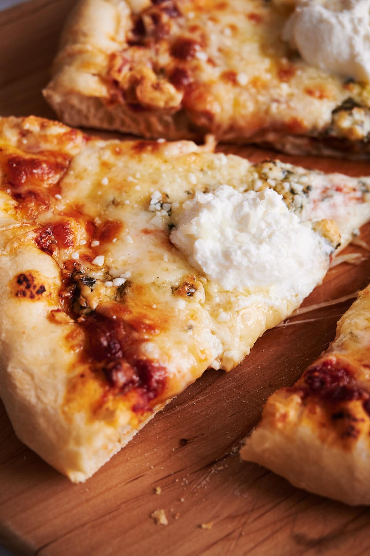 Close up of baked 7 cheese pizza with ricotta on a wooden pizza peel.