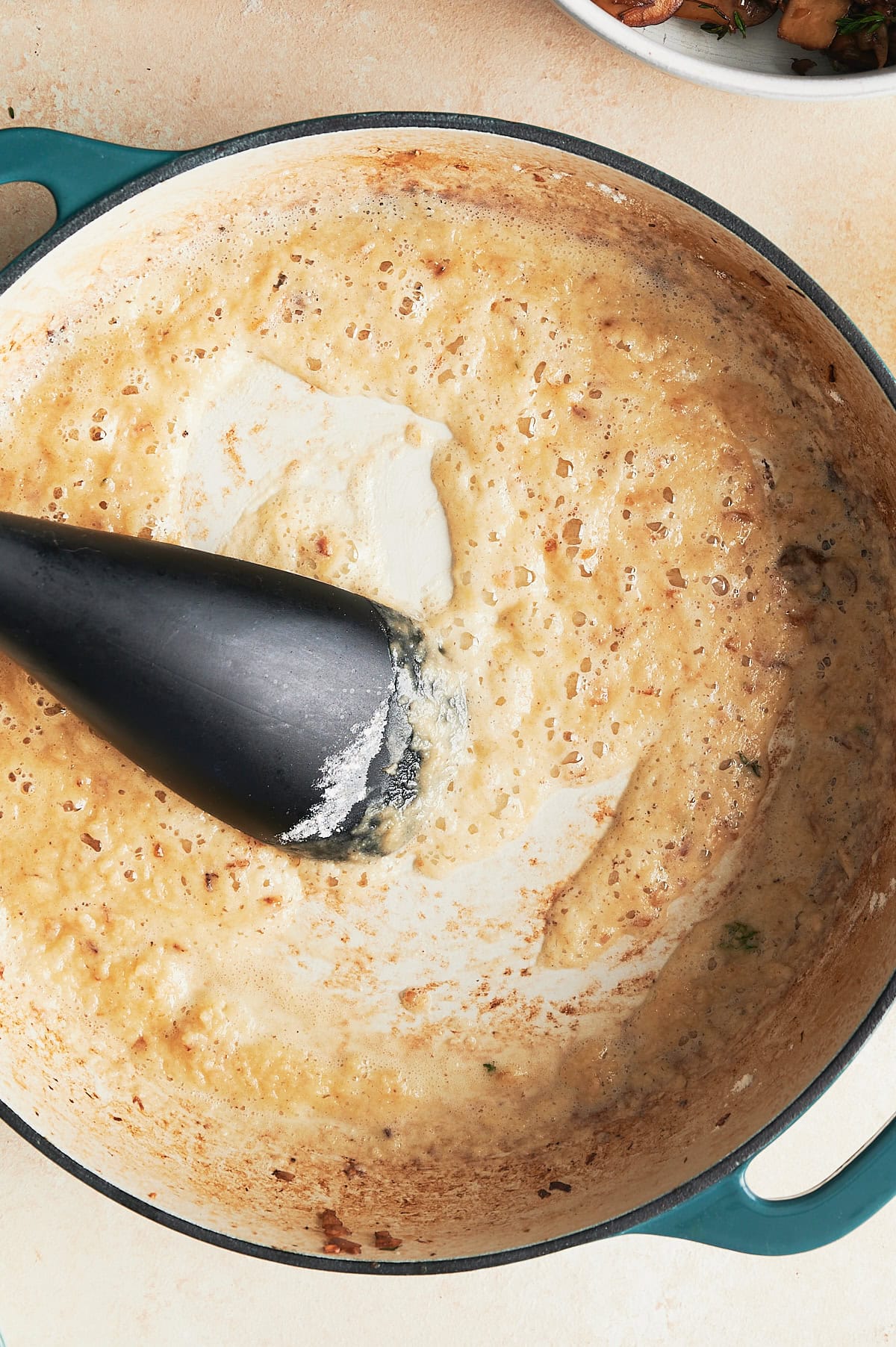 Mushroom roux being stirred by black spatula n a white and blue enameled cast iron pan.