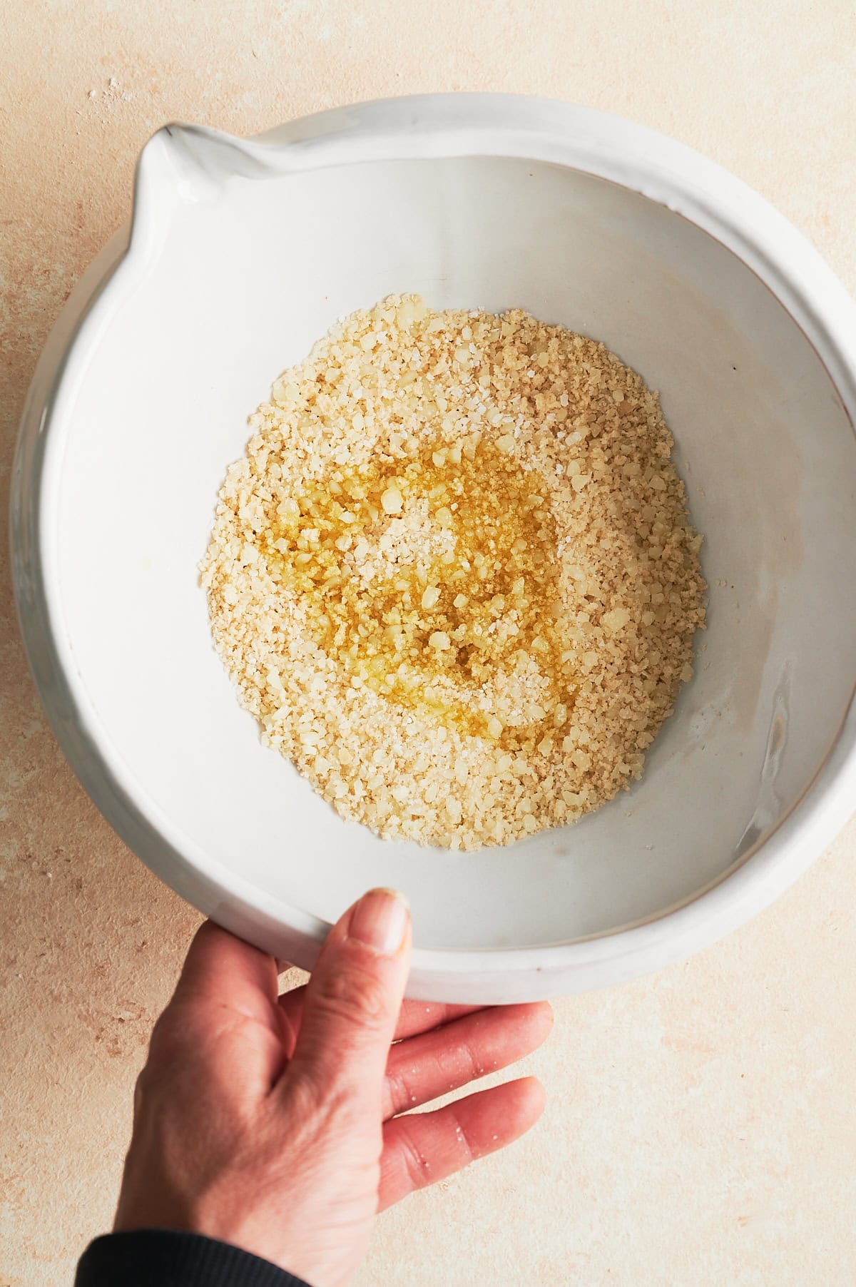 Hand reaching for white bowl with breadcrumb topping ingredients for creamy chicken pasta.