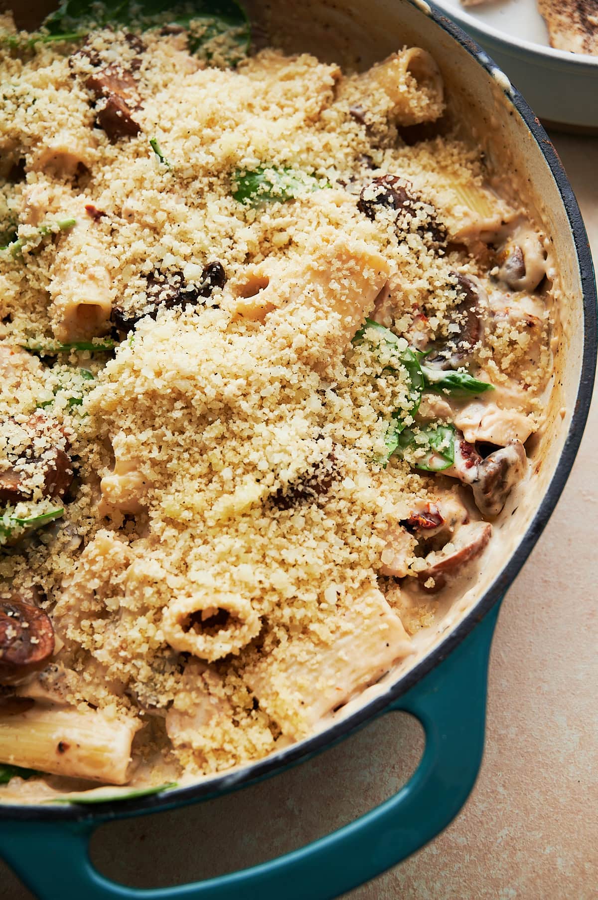 Breadcrumbs on top of unbaked creamy chicken pasta with mushrooms in a white and blue skillet.