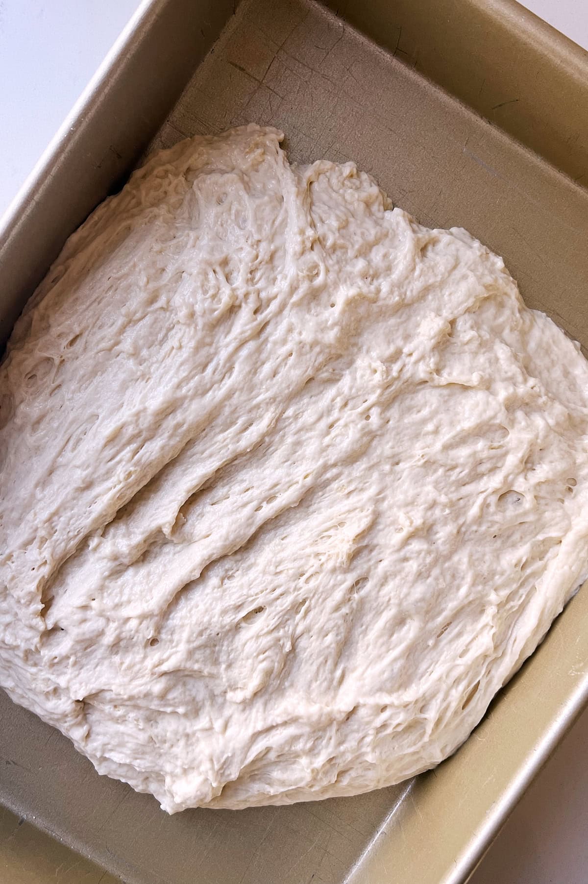 Focaccia dough shaken in pan to shape for cinnamon roll bread.