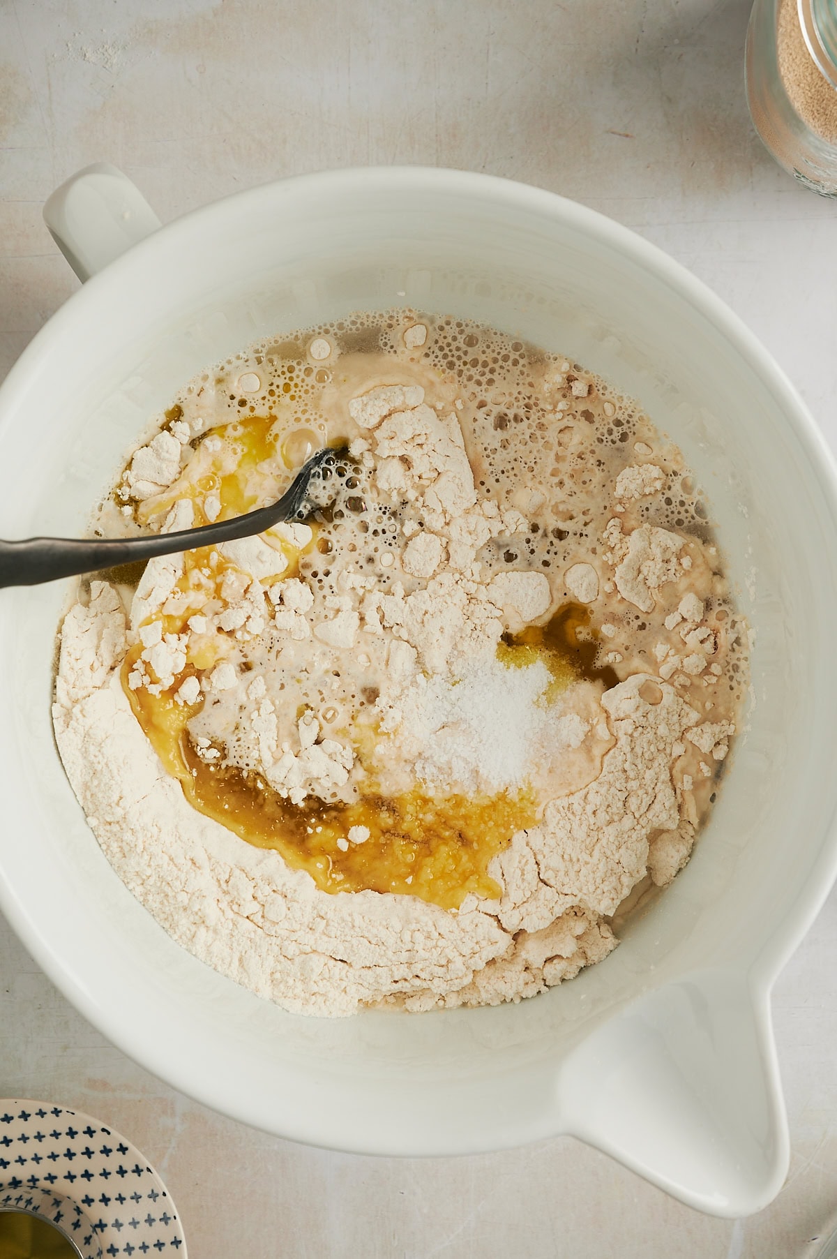 White bowl of oil and water being added to cinnamon focaccia dough being mixed with a fork.
