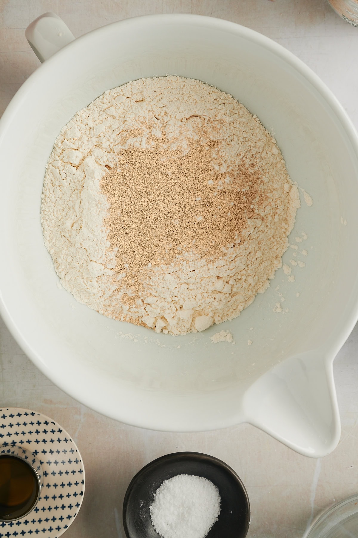 Flour and yeast being mixed in white bowl for cinnamon roll focaccia bread on white background.