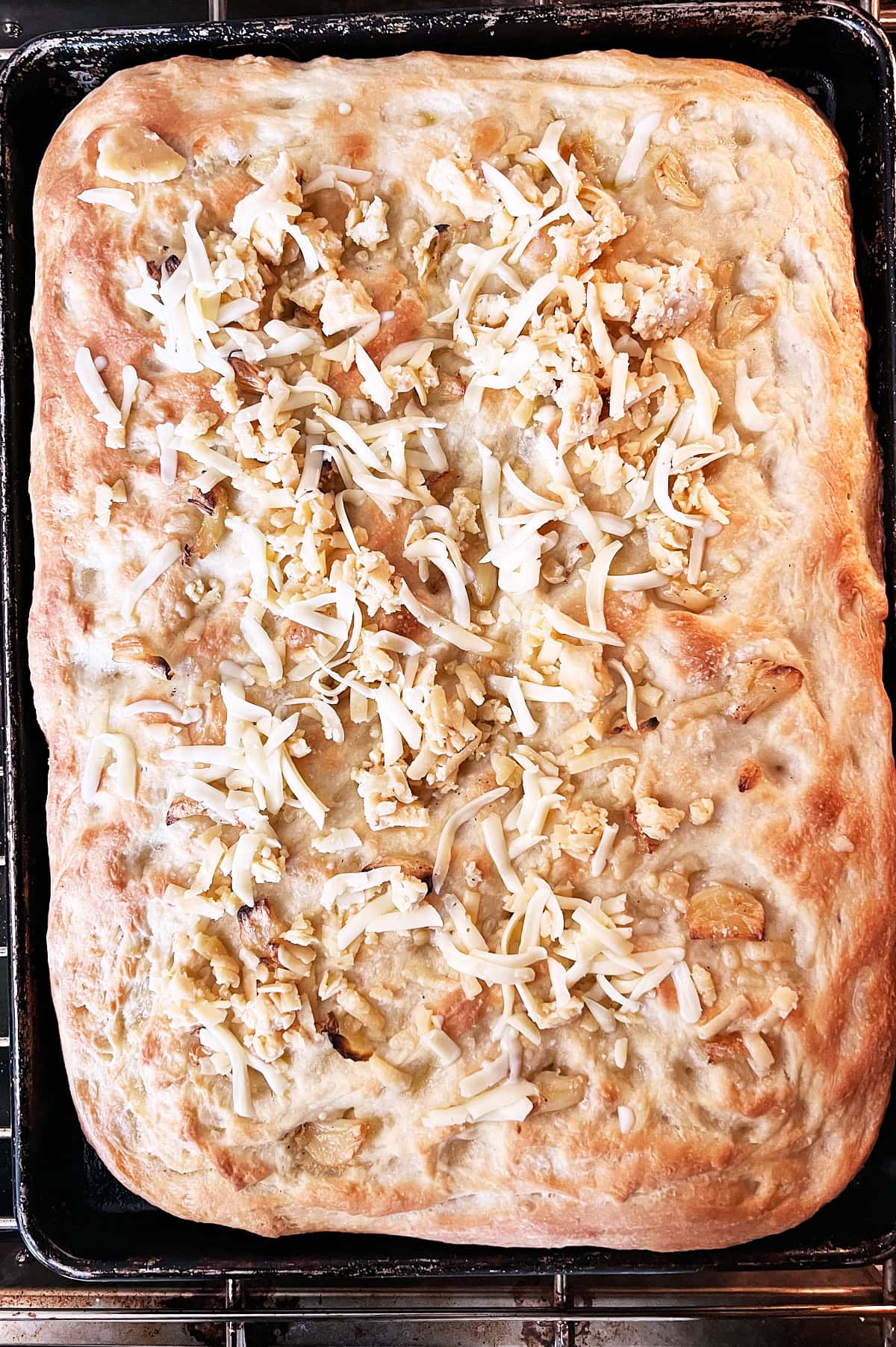 Garlic focaccia bread half baked before and cheese being added on top.