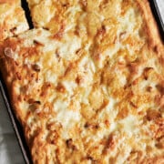 Angled baked pan of cheesy garlic focaccia bread with piece cut out.