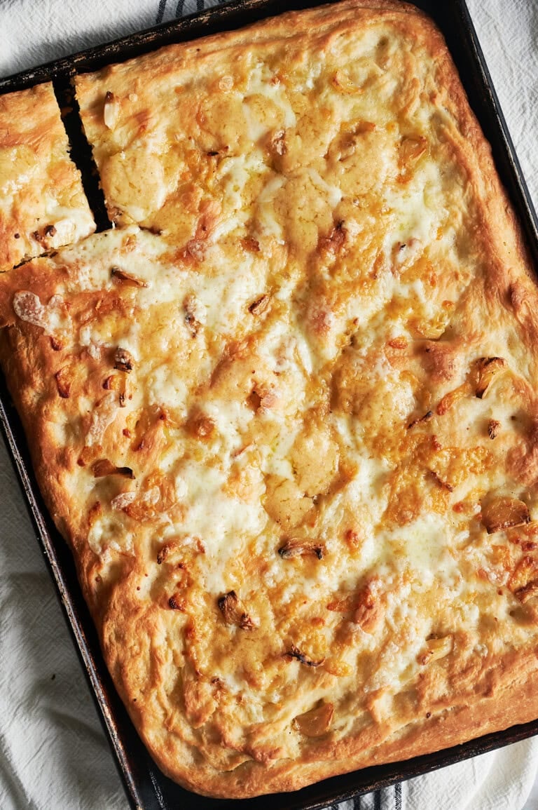 Angled baked pan of cheesy garlic focaccia bread with piece cut out.