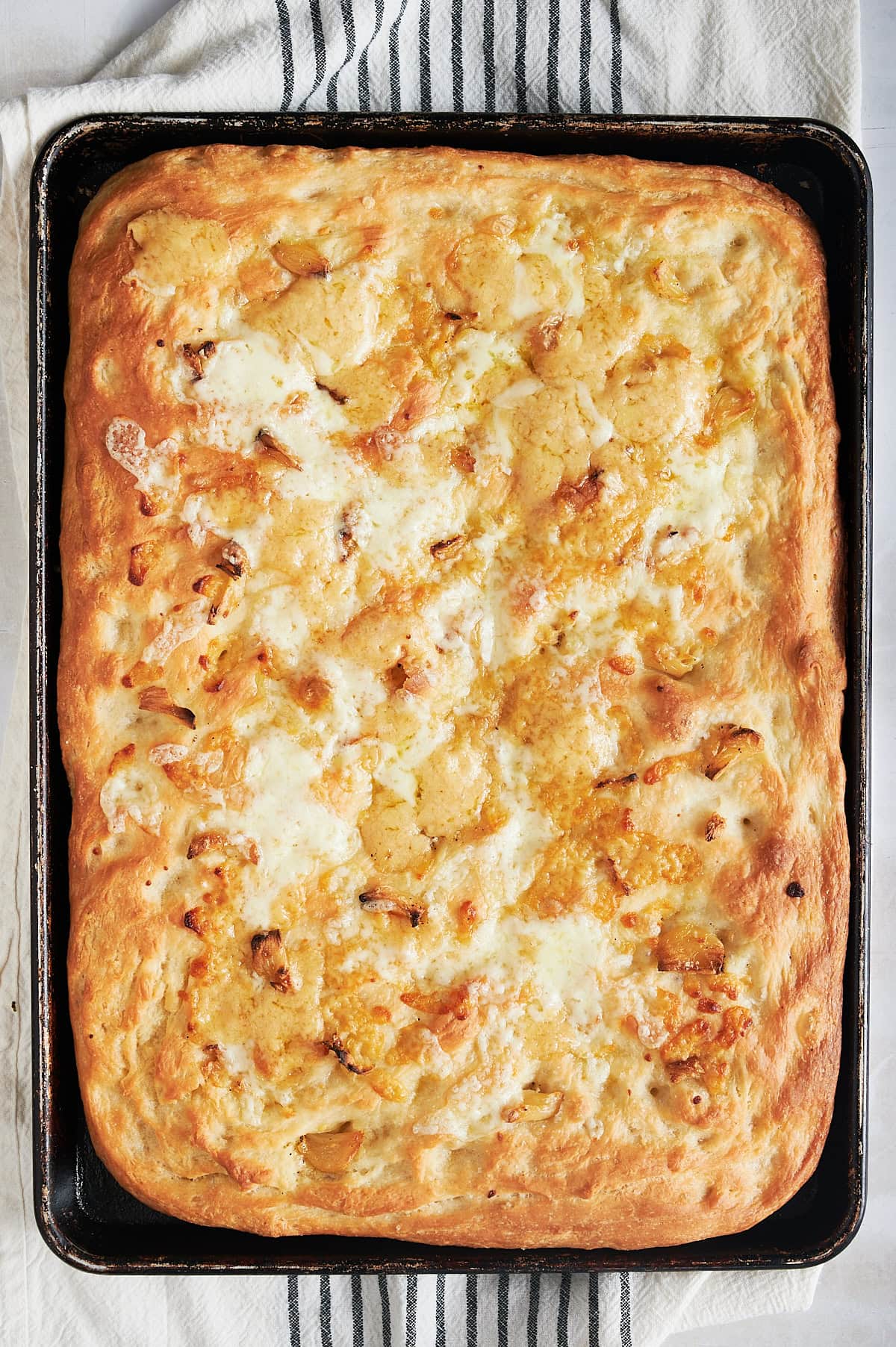 Garlic bread focaccia bread with melted cheese baked in black sheet pan on black and white striped napkin.