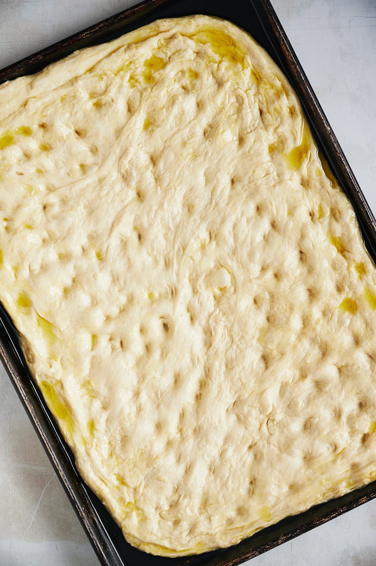 Black sheet plan with unbaked dimpled focaccia bread in oil.
