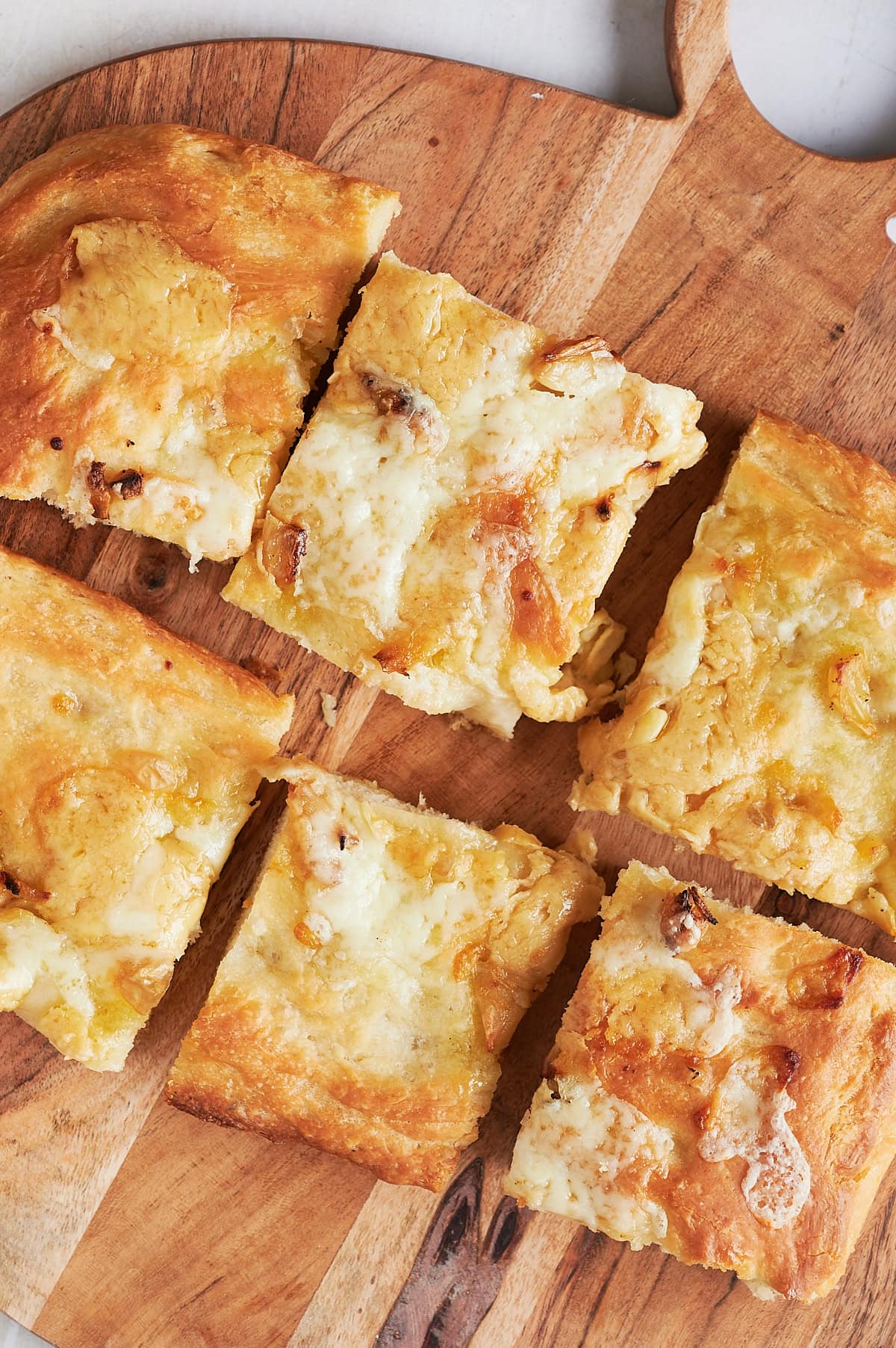 Wooden board of six cut pieces of baked cheese and garlic focaccia bread.