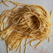 Nest of chitarra pasta on a creamy colored background.
