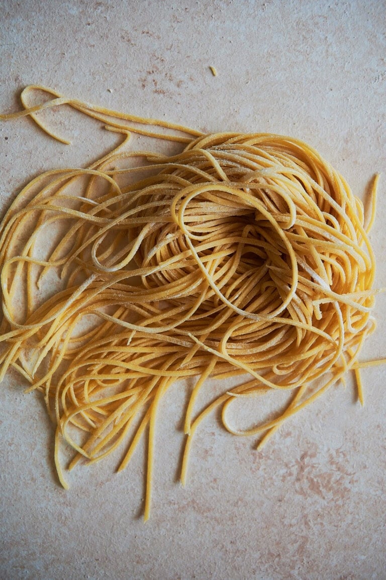 Nest of chitarra pasta on a creamy colored background.