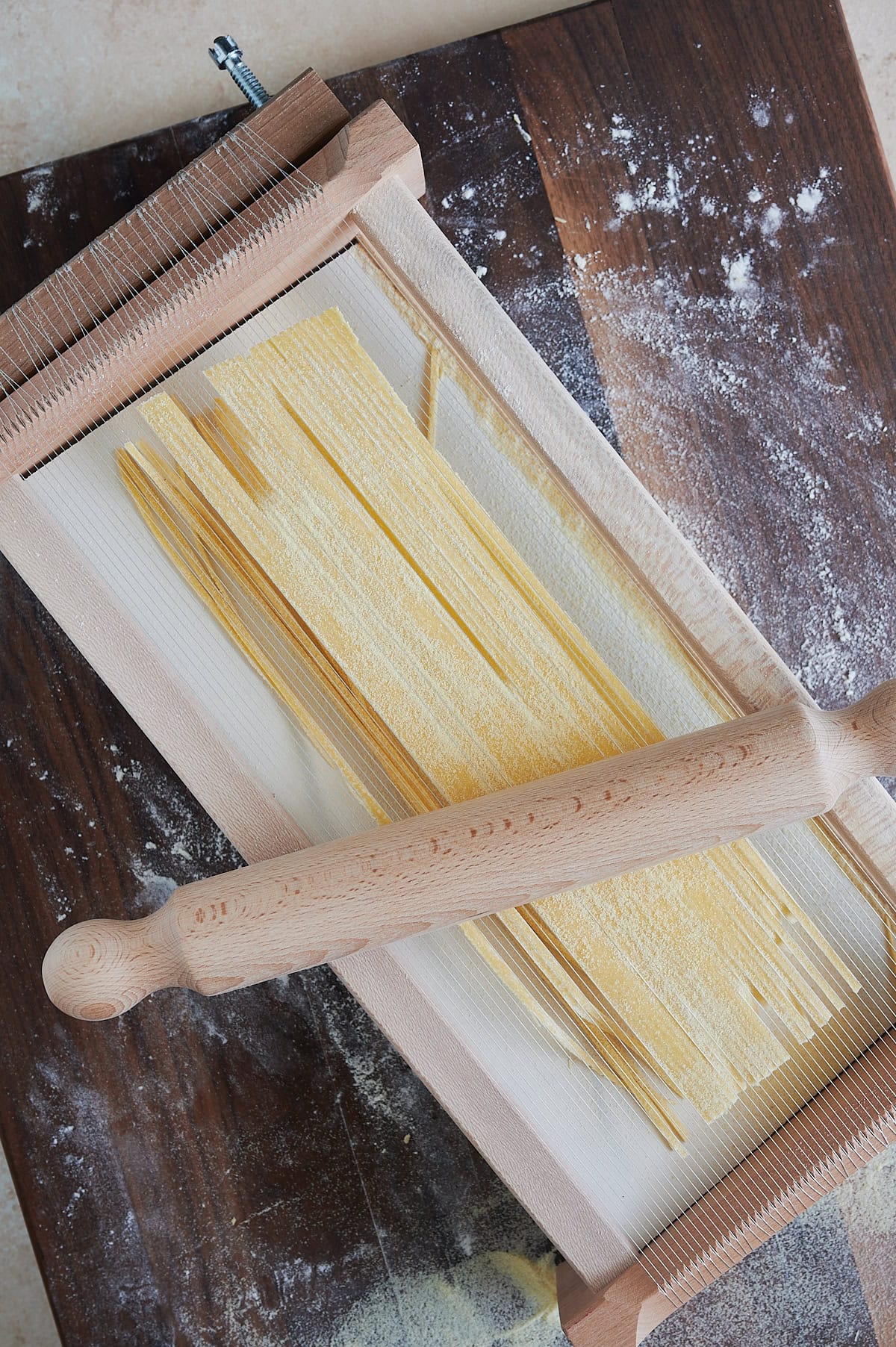 Chitarra pasta being rolled and cut with a small wooden rolling pin on a chitarra machine.