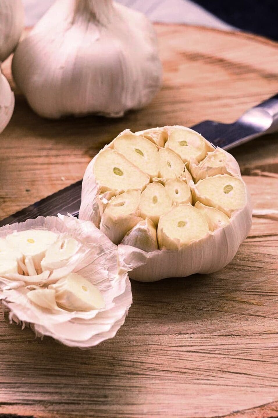 A wooden trivet holding a head of garlic that has been trimmed with a sharp knife to expose the tops of the cloves.