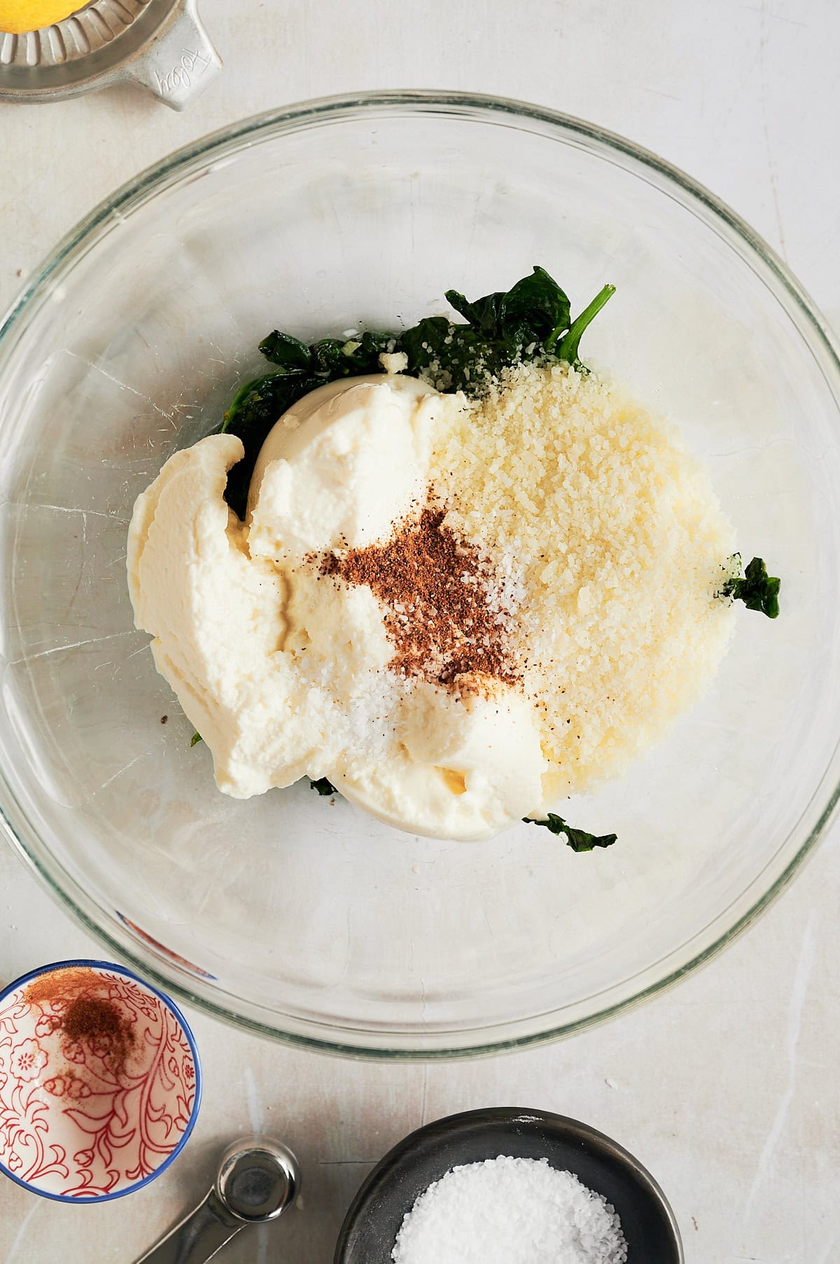 Glass bowl with sauteed spinach, ricotta, parmesan, nutmeg and seasoning for spinach ravioli.