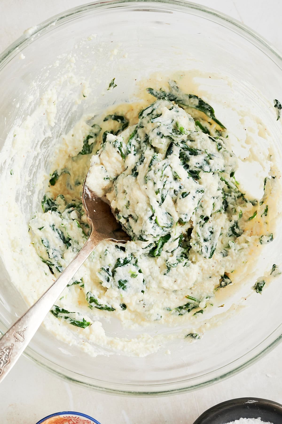 Glass bowl of spinach ricotta filling with a silver spoon.