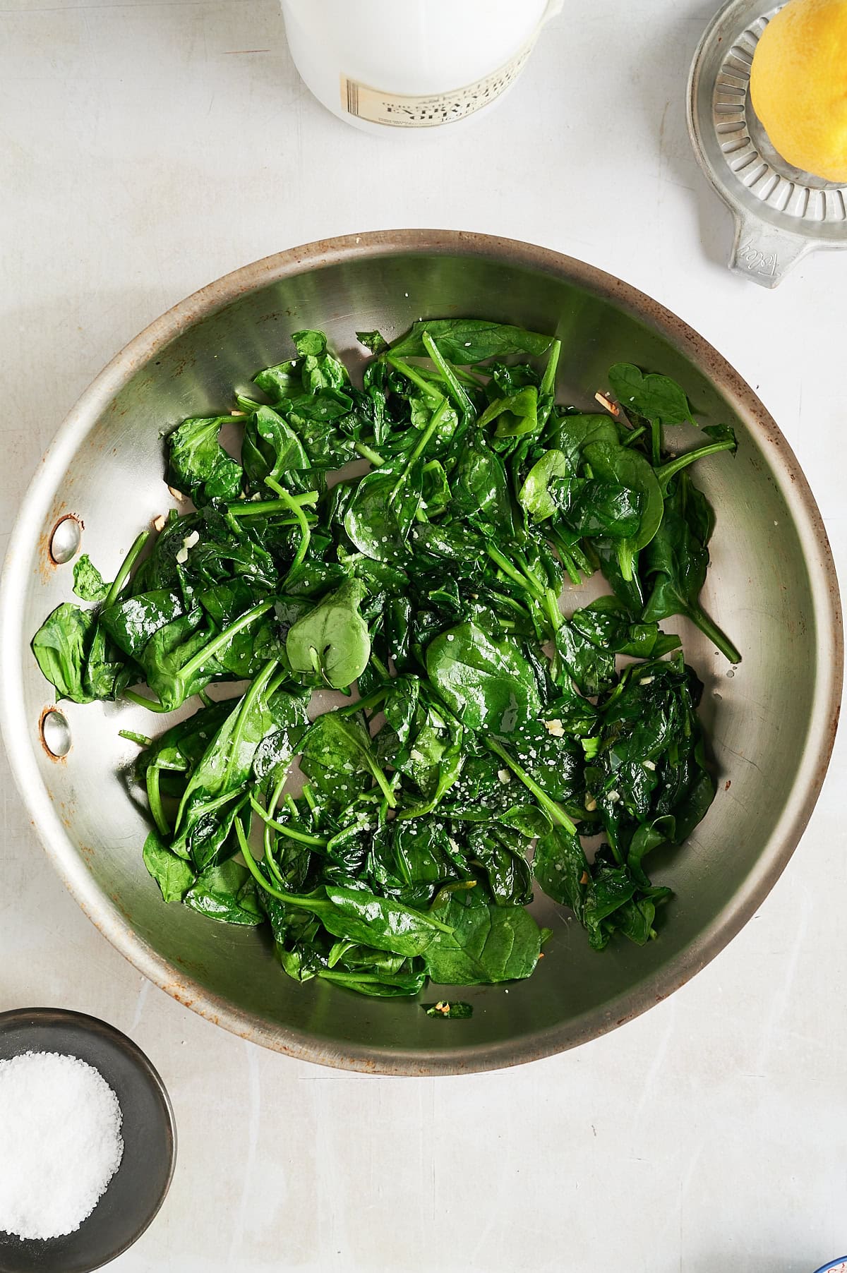 Stainless skillet with sauteed wilted spinach, lemon, and olive oil.