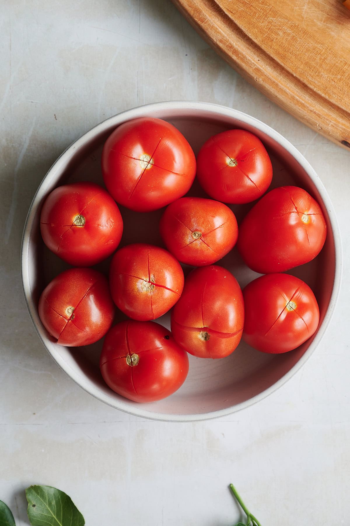 White bowl of Roma tomatoes with x's on top for peeling.