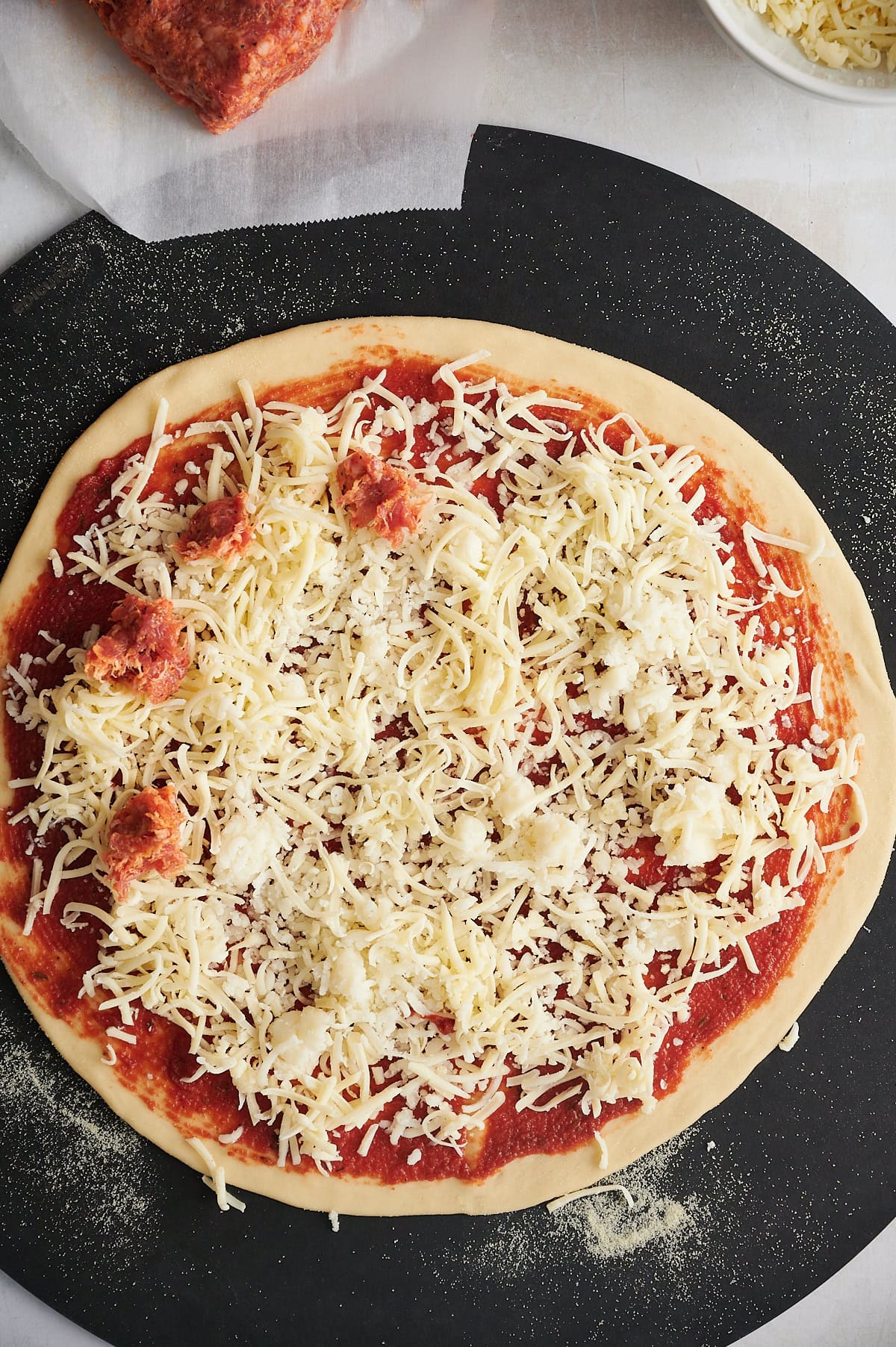 Raw sausage spaced on cheese covered thin crust pizza on black pizza stone.