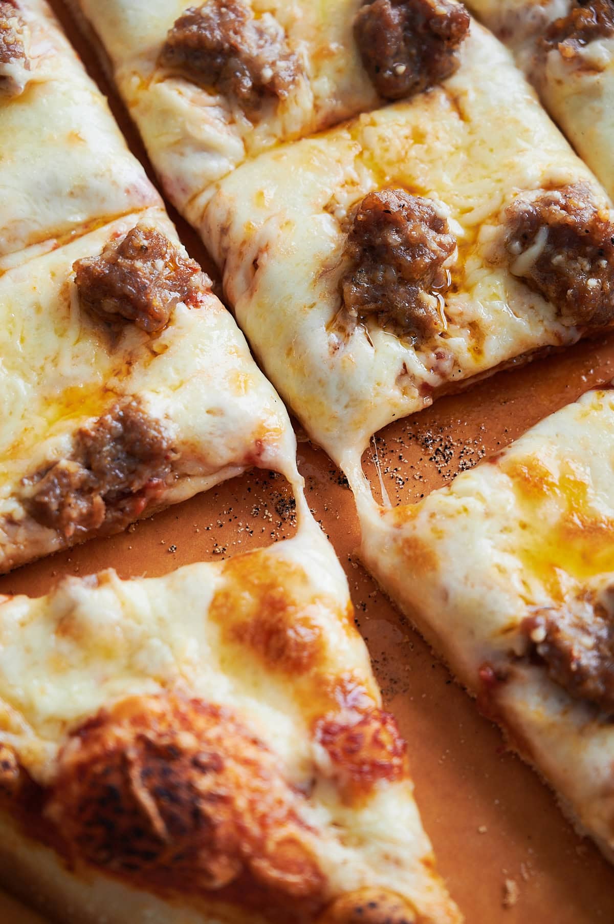 Close up of 4 pieces of thin crust sausage pizza with gooey cheese.