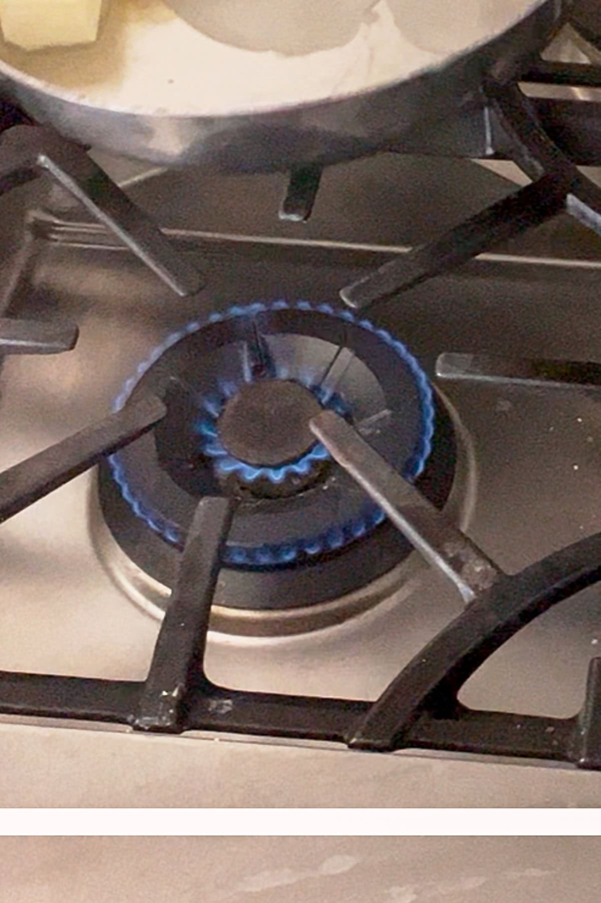 A gas stove burner with a blue flame, partially covered by a pot simmering a rich brown butter pasta sauce.