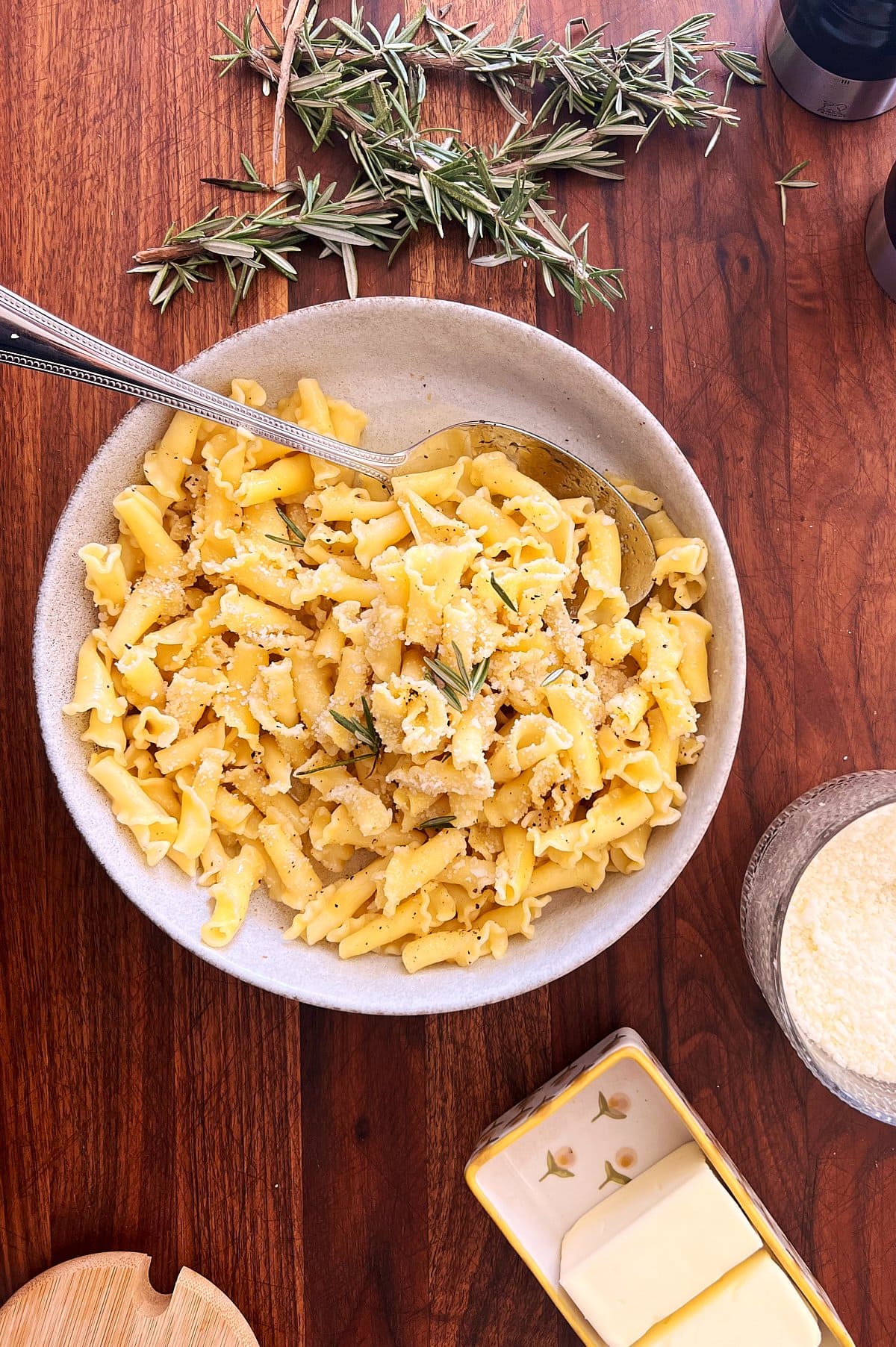 A bowl of pasta with brown butter, herbs and grated cheese sits on a wooden table.