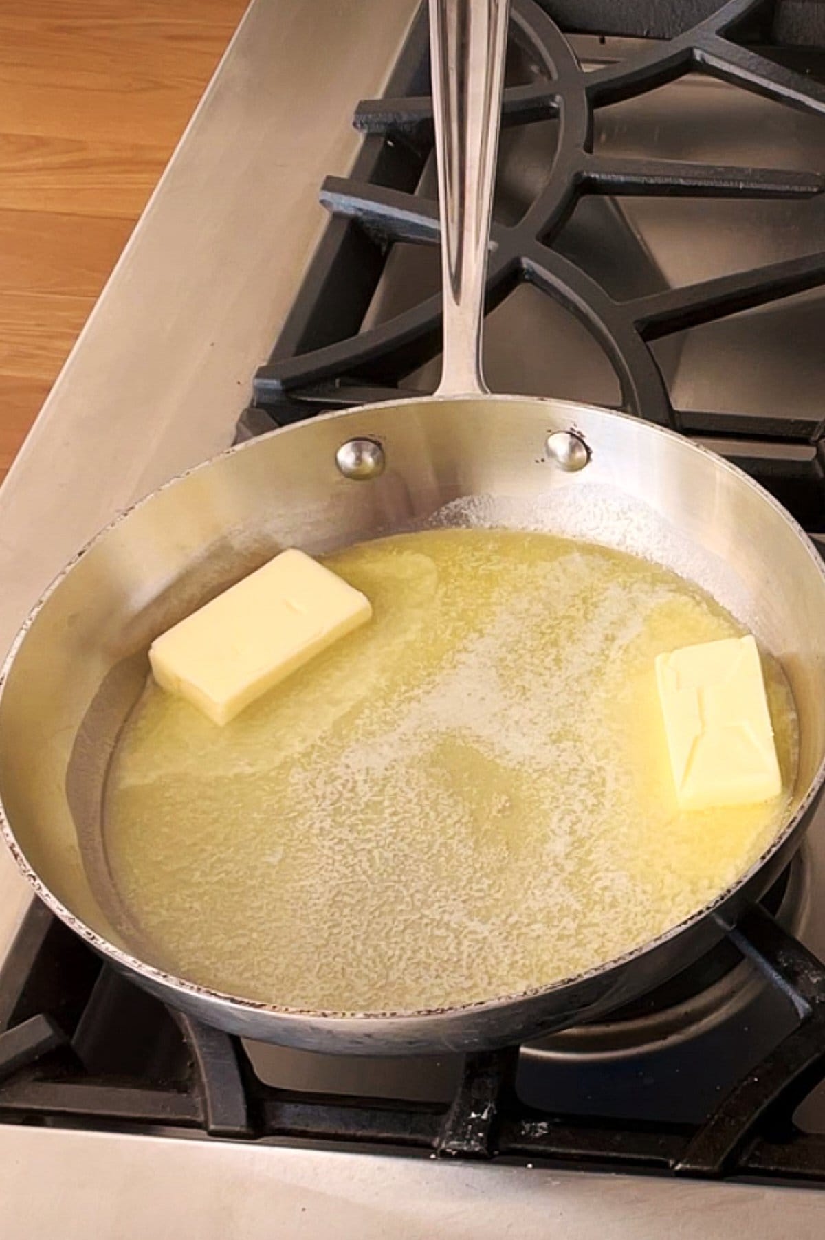 A stainless steel pan on a stove with two chunks of butter partially melted, surrounded by melted butter.