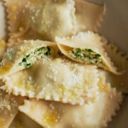 Close up of a white bowl of cooked chicken ravioli drizzled with olive oil and sprinkled with parmesan.