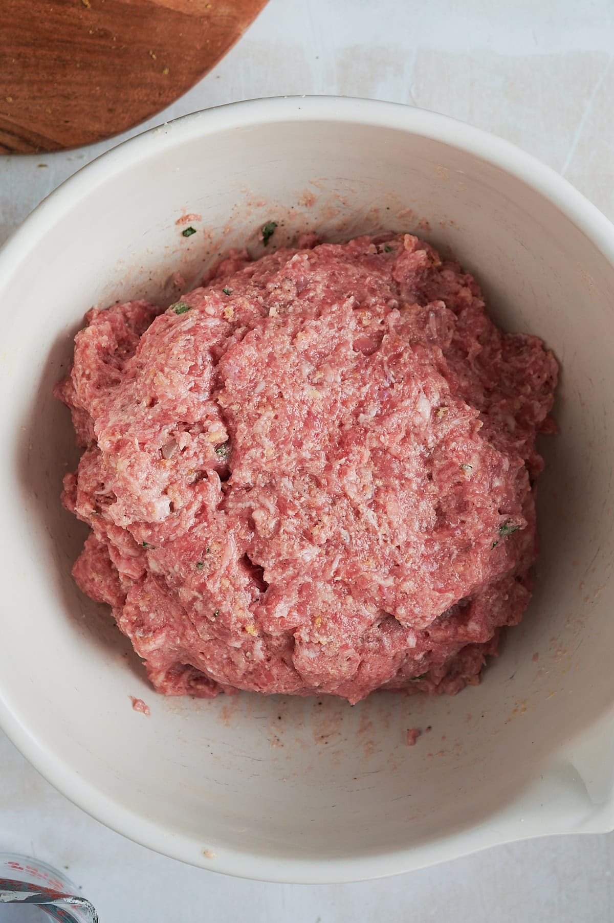 White bowl of mixed meat for giant Italian meatballs sitting on a white background.