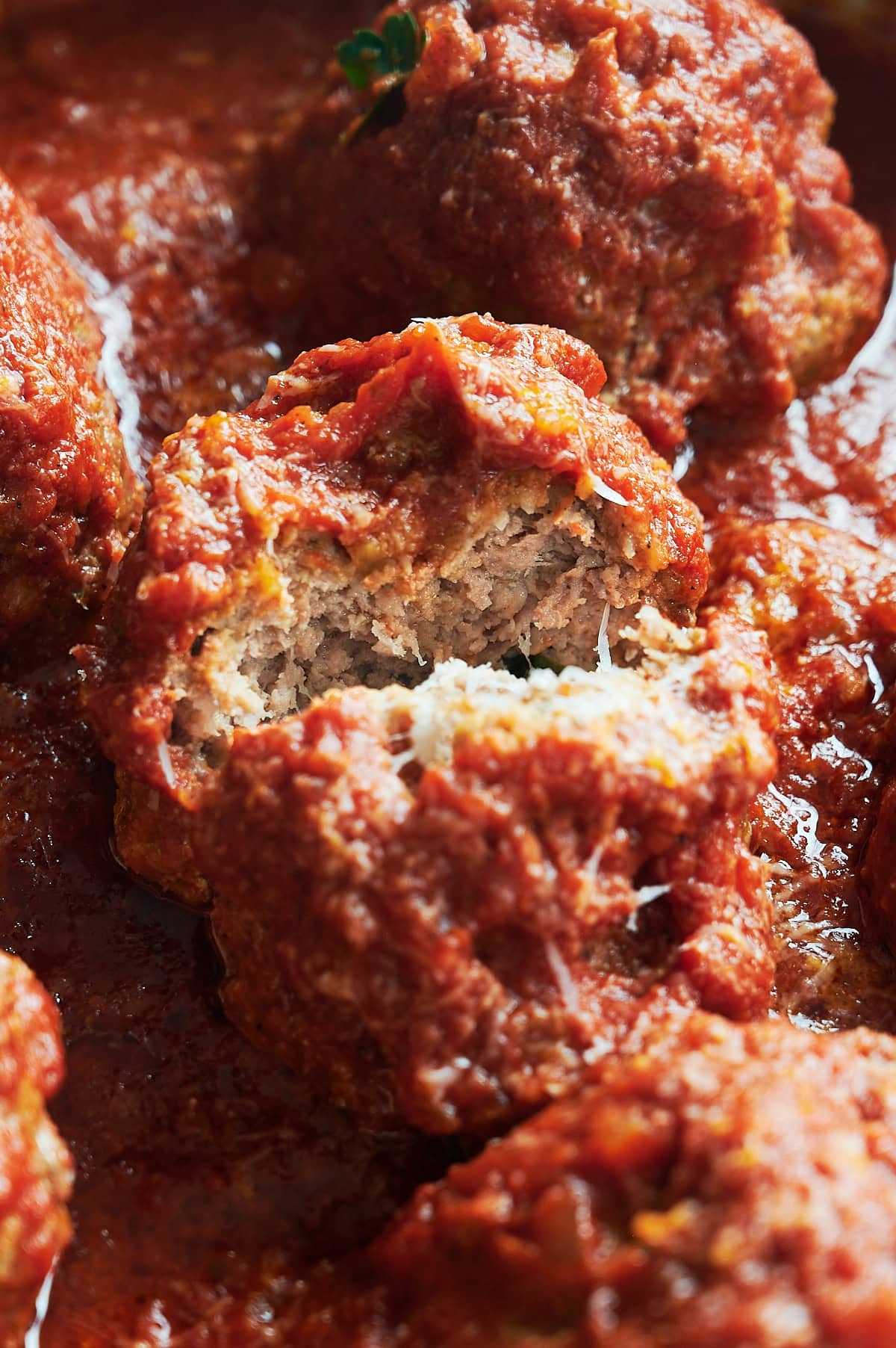 Close-up of meatballs in rich tomato sauce, with one meatball split open to reveal its juicy, tender interior.