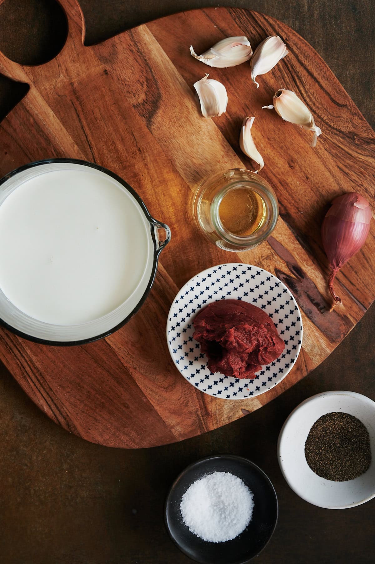 Wooden board with bowls of cream, tomato paste, white wine, garlic, shallots and small bowls of salt and pepper.